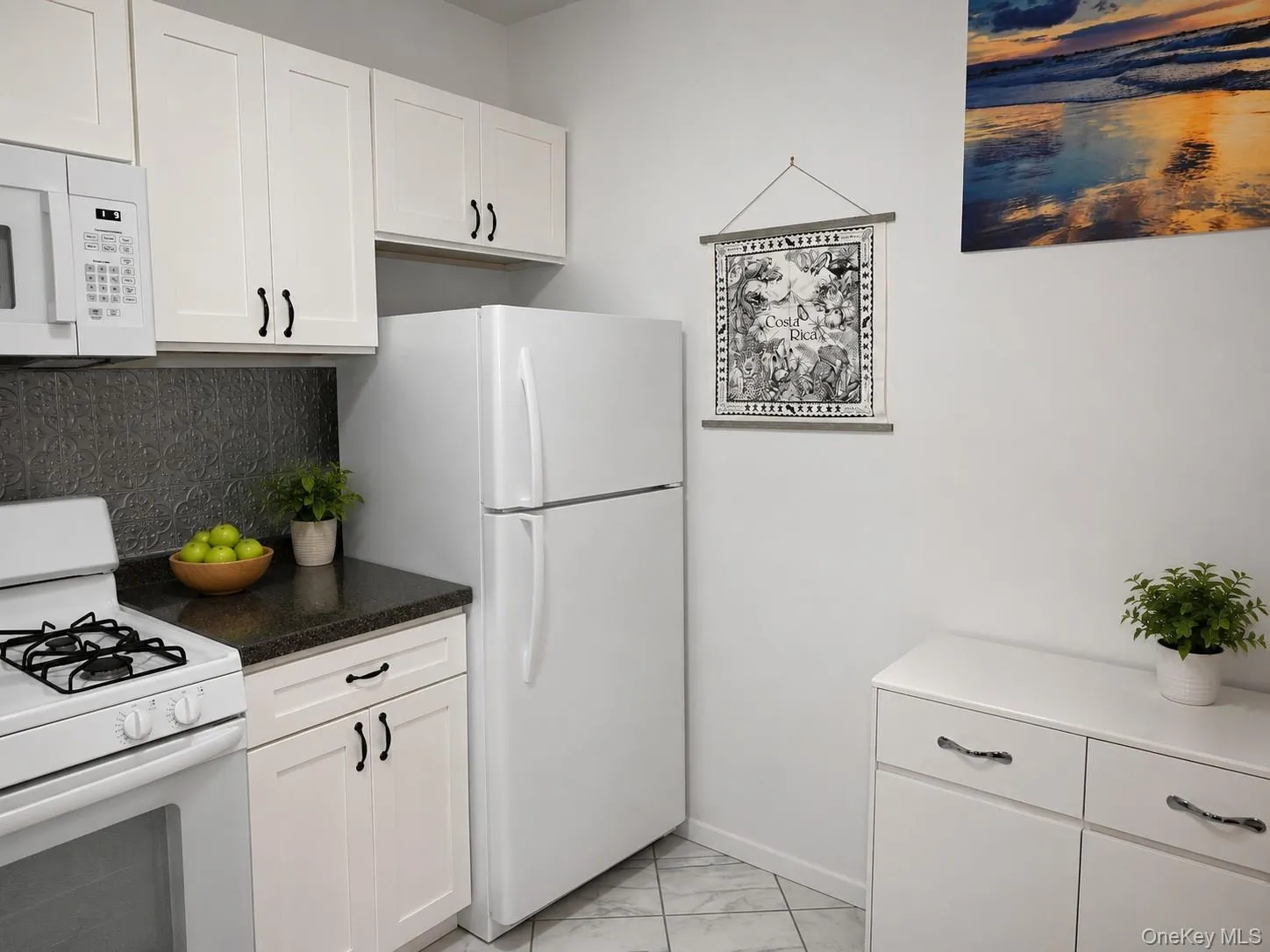 Modern kitchen featuring white cabinetry with black hardware, a dark patterned backsplash, and granite-finish countertops( virtually staged) Modern kitchen featuring white cabinetry with black hardware, a dark patterned backsplash, and granite-finish countertops( virtually staged)