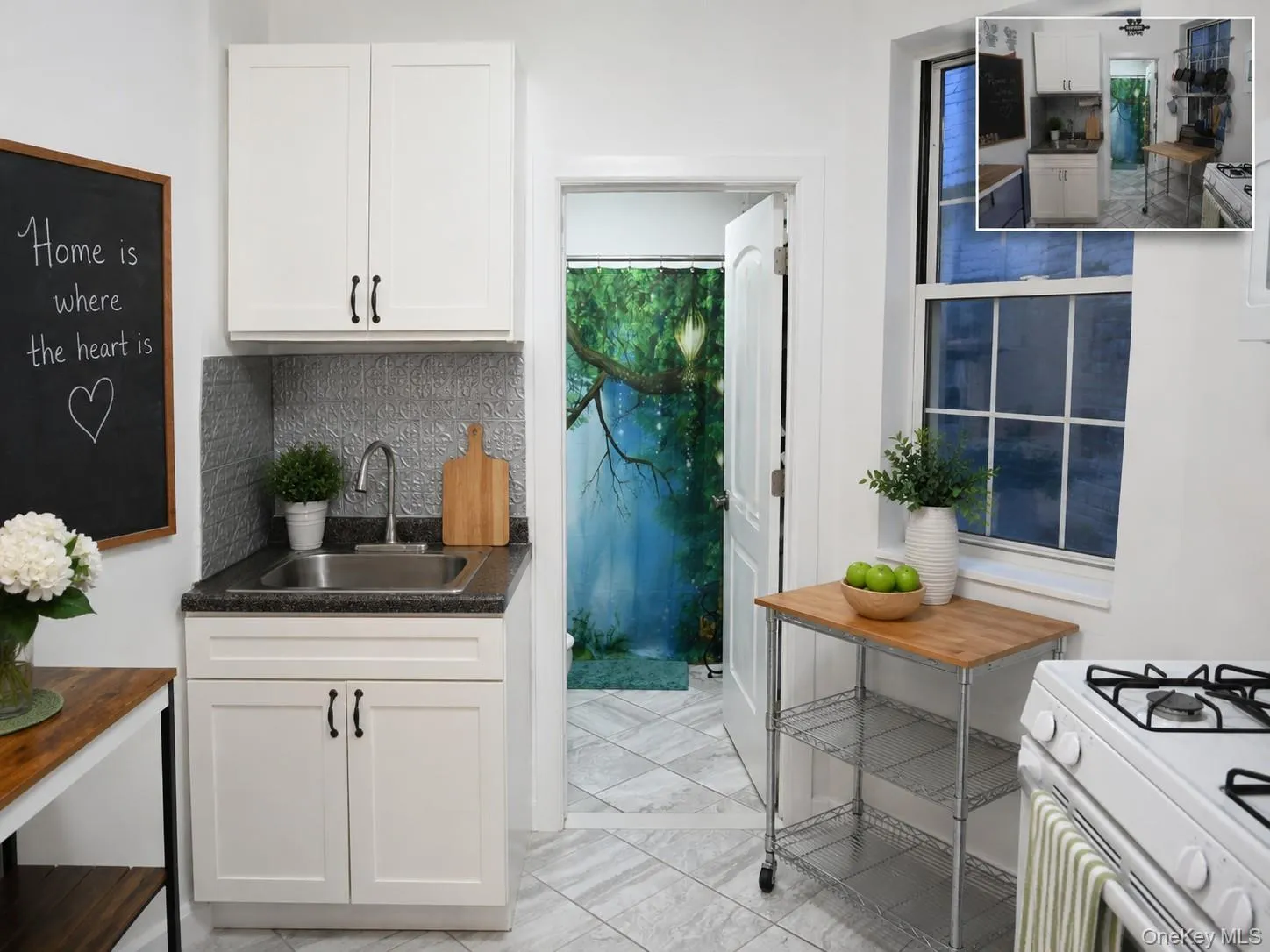 Compact kitchen featuring white cabinetry, a stainless steel sink, and a textured backsplash (virtually staged) Compact kitchen featuring white cabinetry, a stainless steel sink, and a textured backsplash (virtually staged)