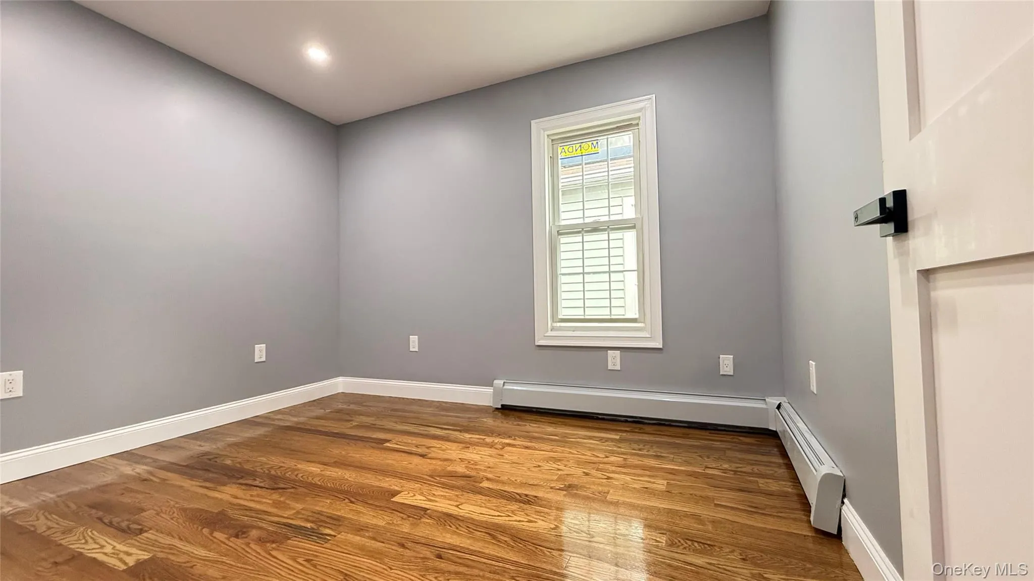 Room featuring hardwood flooring, light grey painted walls, recessed ceiling lighting, baseboard trim, and a window with white trim Room featuring hardwood flooring, light grey painted walls, recessed ceiling lighting, baseboard trim, and a window with white trim