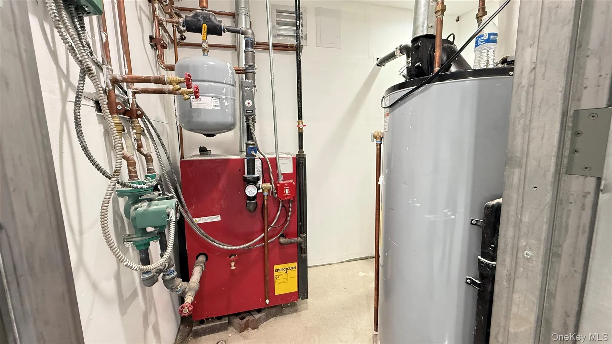 Mechanical room featuring a red heating unit, copper piping, an expansion tank, and a grey water heater Mechanical room featuring a red heating unit, copper piping, an expansion tank, and a grey water heater