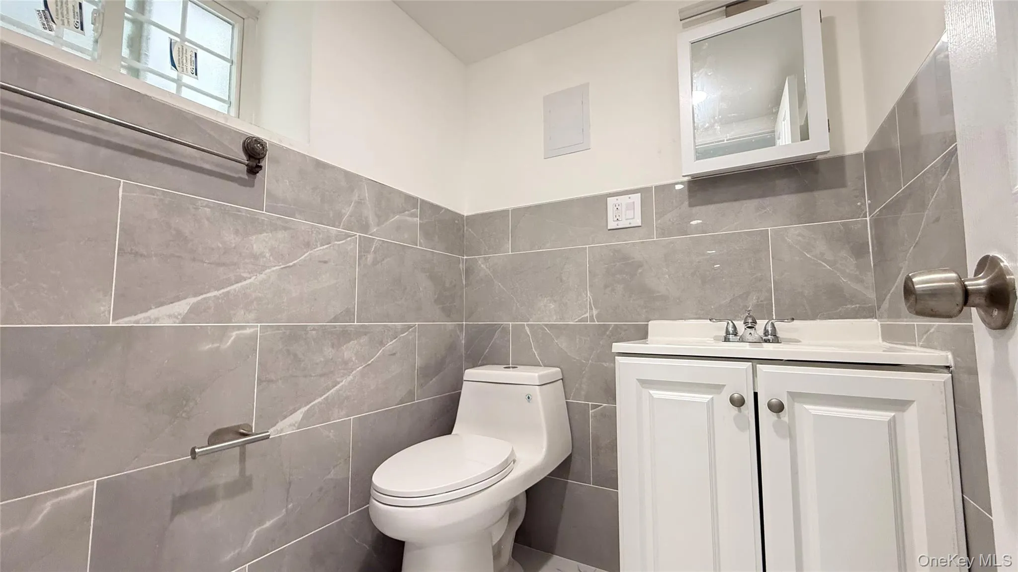 Bathroom featuring full-height gray tile walls, a white vanity with an integrated sink, and a mirrored medicine cabinet Bathroom featuring full-height gray tile walls, a white vanity with an integrated sink, and a mirrored medicine cabinet