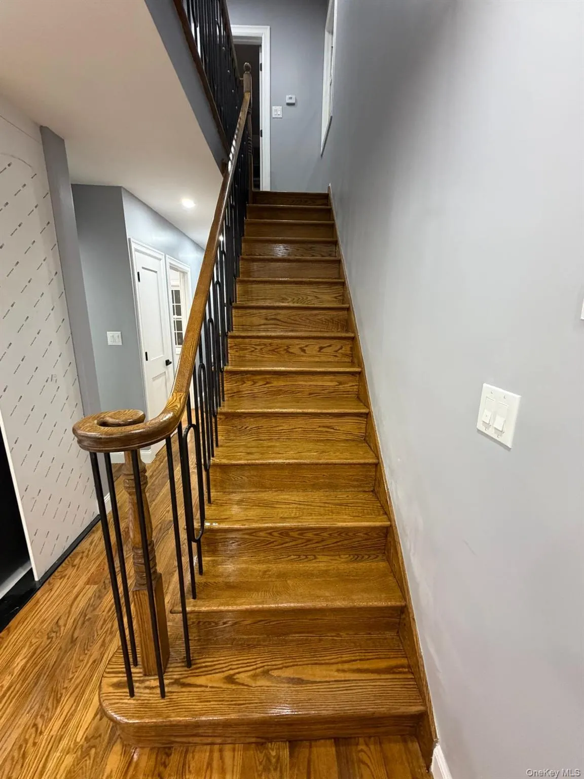 Hardwood staircase featuring a natural wood finish, black metal balusters, and a curved wooden handrail Hardwood staircase featuring a natural wood finish, black metal balusters, and a curved wooden handrail