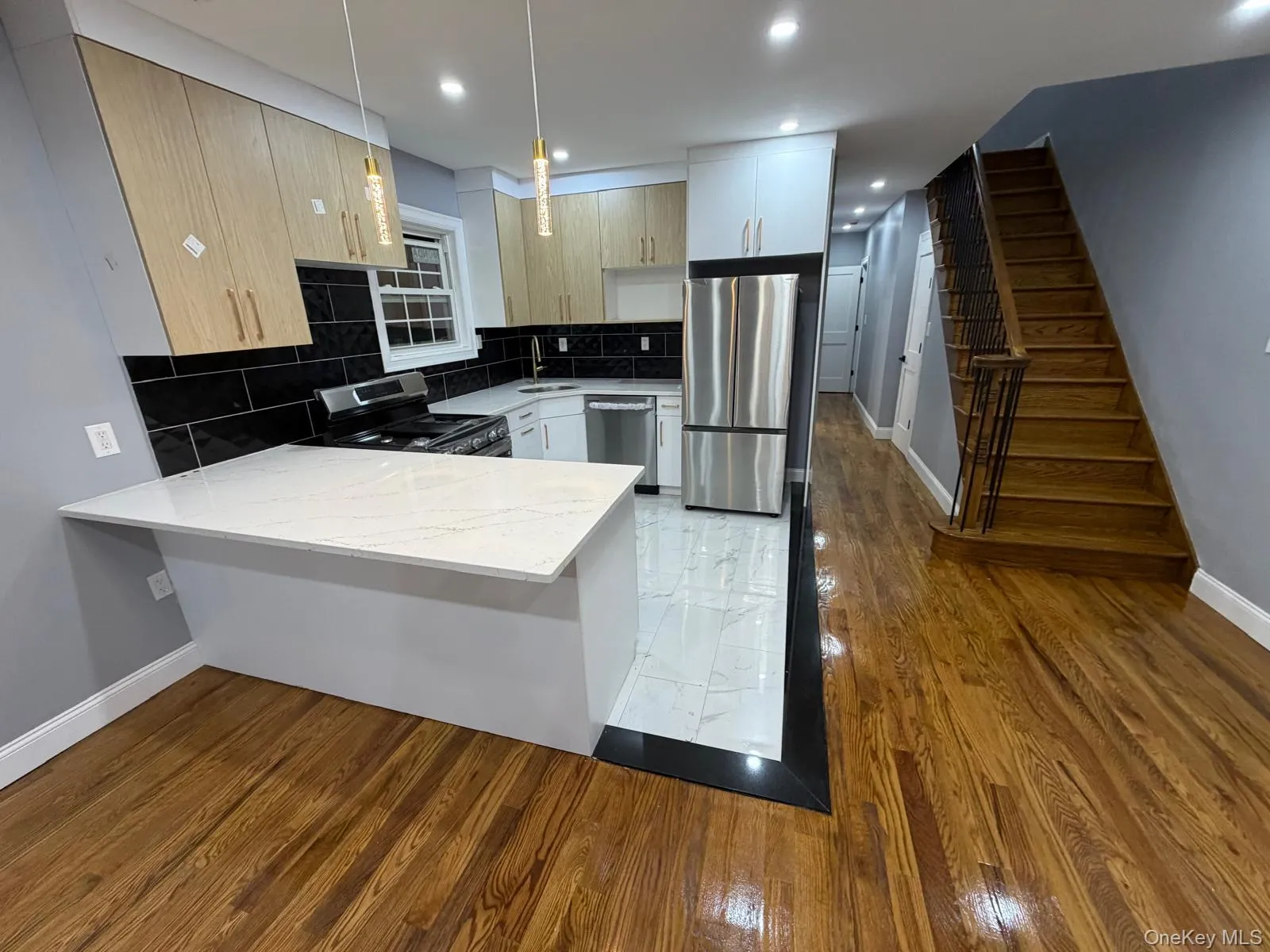 Kitchen featuring a quartz-top peninsula, stainless steel appliances, black subway tile backsplash, light wood-finish cabinetry, and recessed lighting Kitchen featuring a quartz-top peninsula, stainless steel appliances, black subway tile backsplash, light wood-finish cabinetry, and recessed lighting