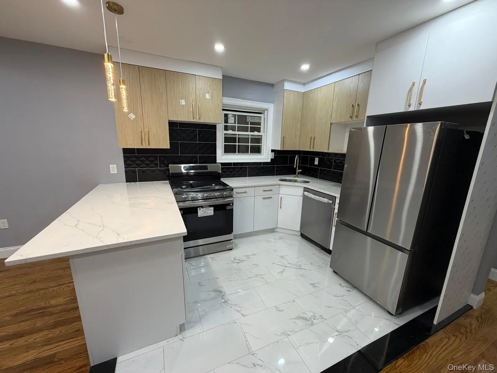Modern kitchen featuring stainless steel appliances, a white quartz countertop, two-tone cabinetry, a black subway tile backsplash, and a gold-finish pendant light fixture Modern kitchen featuring stainless steel appliances, a white quartz countertop, two-tone cabinetry, a black subway tile backsplash, and a gold-finish pendant light fixture