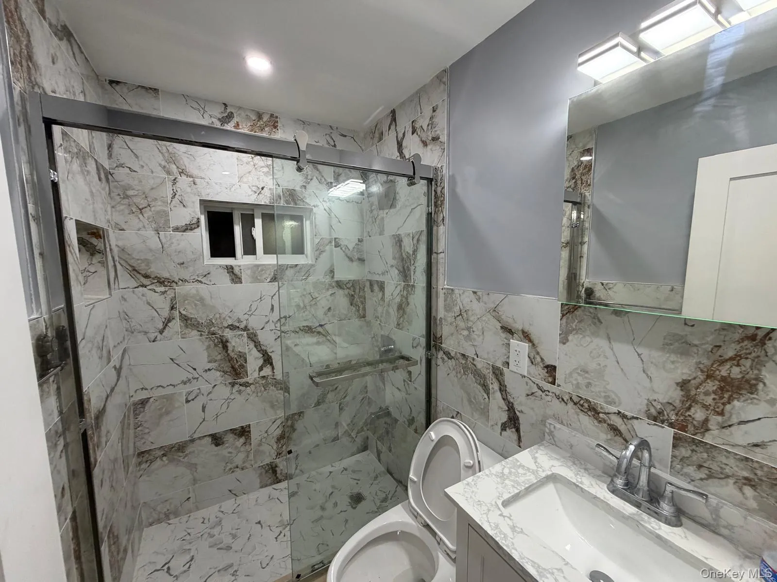 Modern bathroom featuring a tiled shower enclosure with glass sliding doors, a built-in shower niche, and a frosted window Modern bathroom featuring a tiled shower enclosure with glass sliding doors, a built-in shower niche, and a frosted window
