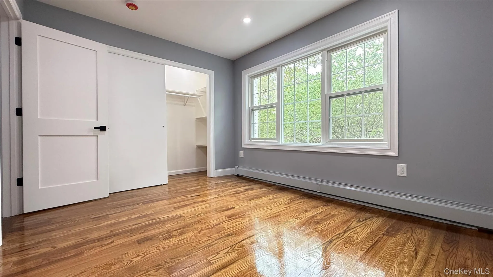 Hardwood flooring, gray wall paint, recessed lighting, white trim windows, and a built-in closet with shelving Hardwood flooring, gray wall paint, recessed lighting, white trim windows, and a built-in closet with shelving