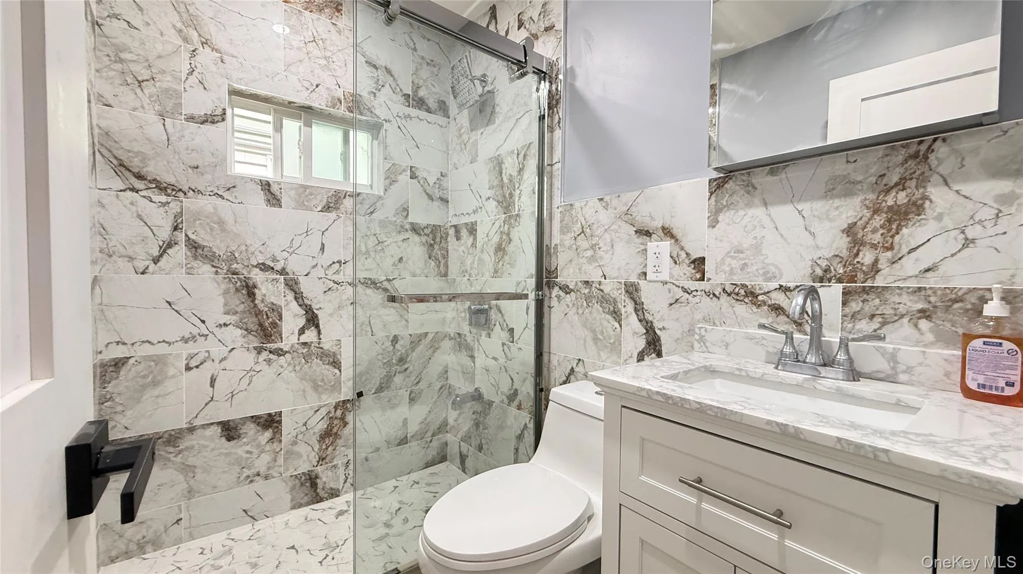 Contemporary bathroom featuring a glass-enclosed shower with a sliding door, white and brown patterned tilework, a white vanity with a light-colored countertop, and a recessed medicine cabinet Contemporary bathroom featuring a glass-enclosed shower with a sliding door, white and brown patterned tilework, a white vanity with a light-colored countertop, and a recessed medicine cabinet