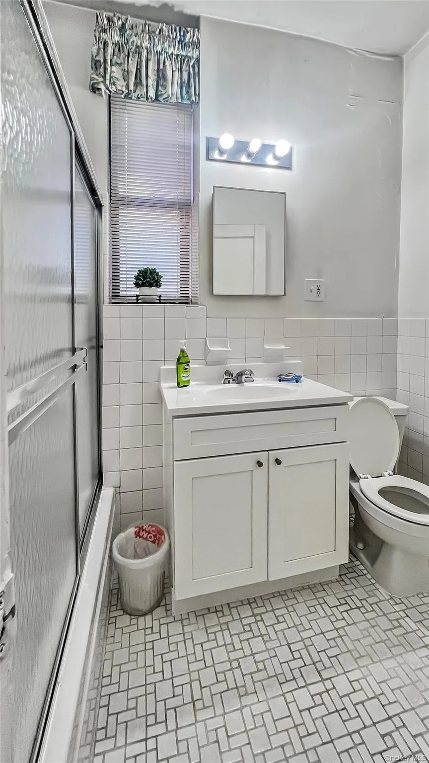 Full bathroom featuring vanity, tile walls, shower / bath combination with glass door, and toilet Full bathroom featuring vanity, tile walls, shower / bath combination with glass door, and toilet
