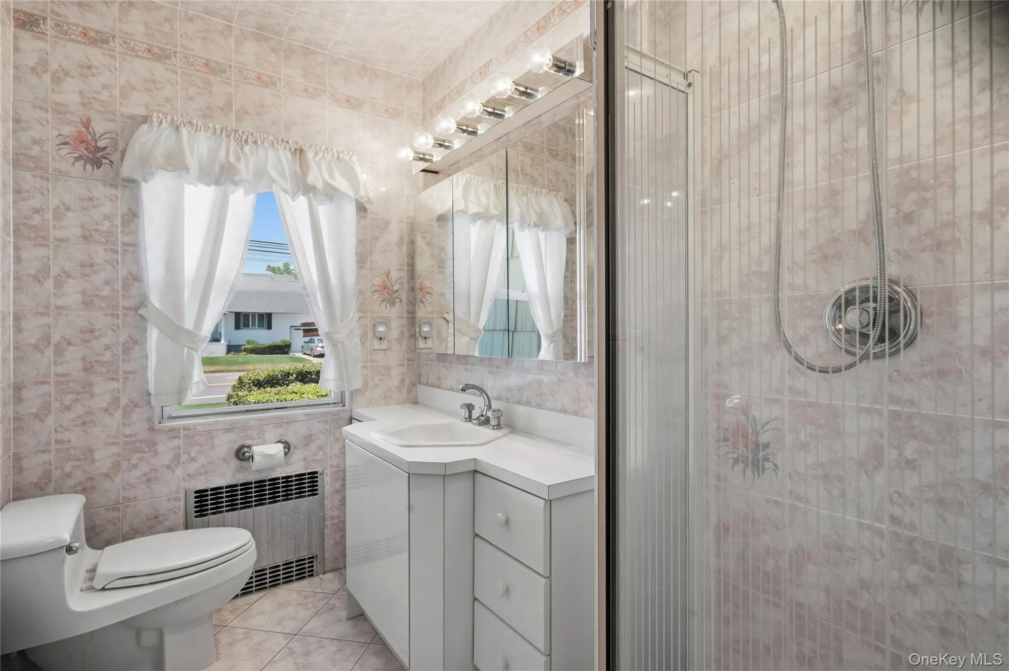 Bathroom featuring a corner vanity with an integrated sink, mirrored medicine cabinet, and a tiled shower enclosure with a glass door Bathroom featuring a corner vanity with an integrated sink, mirrored medicine cabinet, and a tiled shower enclosure with a glass door