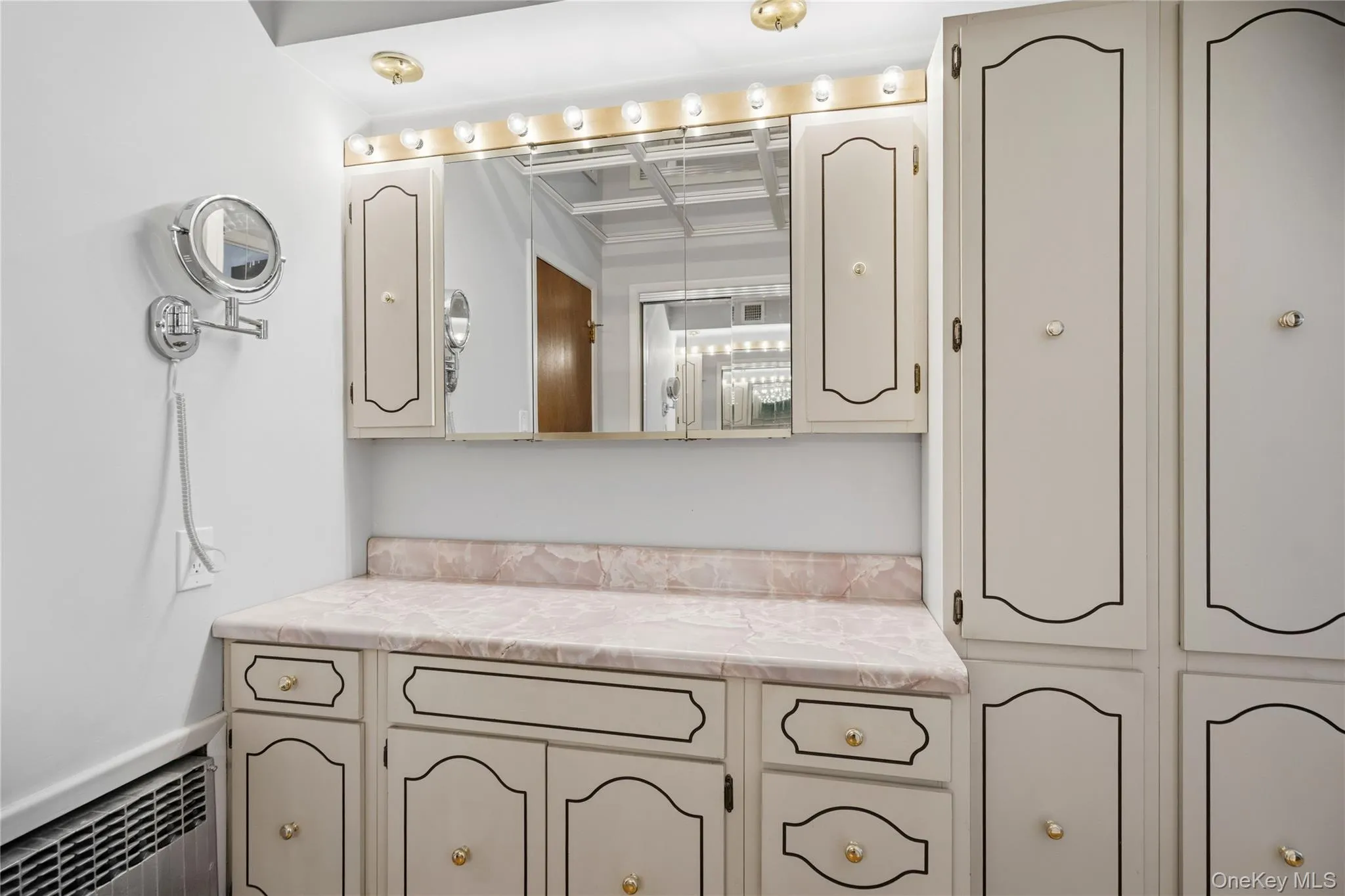 Vanity area with a pink marble-finish countertop, under-counter cabinetry, and a mirrored medicine cabinet with integrated lighting Vanity area with a pink marble-finish countertop, under-counter cabinetry, and a mirrored medicine cabinet with integrated lighting