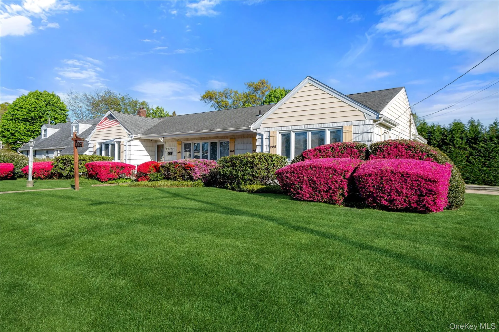 Siding exterior with multiple windows, featuring a meticulously maintained front lawn and vibrant flowering shrubs in varying shades of red and pink Siding exterior with multiple windows, featuring a meticulously maintained front lawn and vibrant flowering shrubs in varying shades of red and pink