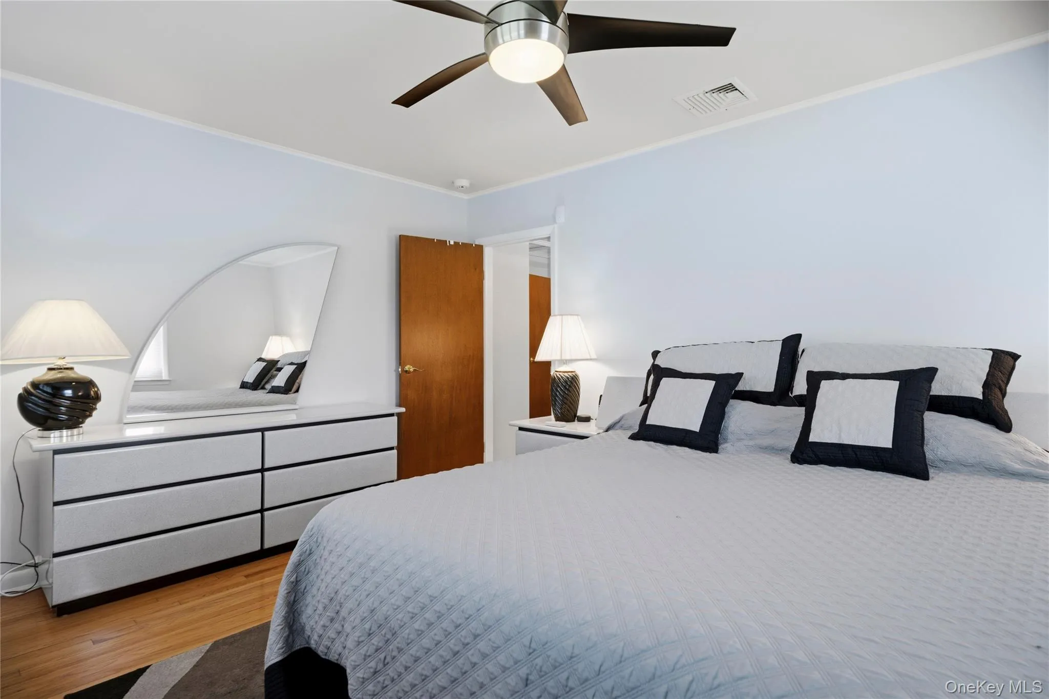 Bedroom featuring wood-finish flooring, a ceiling fan with integrated lighting, white baseboards, and a solid core door Bedroom featuring wood-finish flooring, a ceiling fan with integrated lighting, white baseboards, and a solid core door