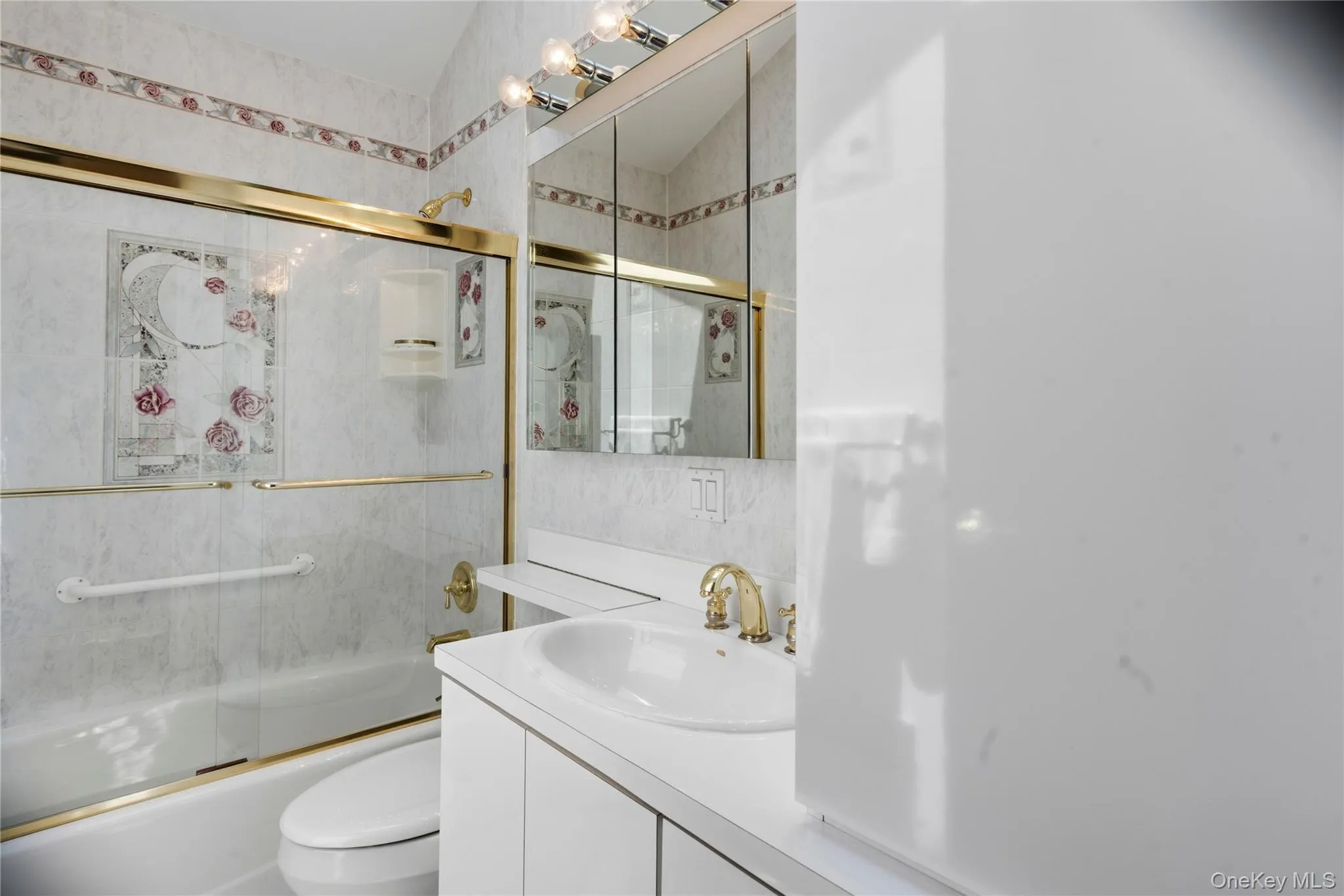 Bathroom featuring a vanity with an integrated sink, gold-tone fixtures, a built-in medicine cabinet, and a bathtub with a sliding glass door Bathroom featuring a vanity with an integrated sink, gold-tone fixtures, a built-in medicine cabinet, and a bathtub with a sliding glass door