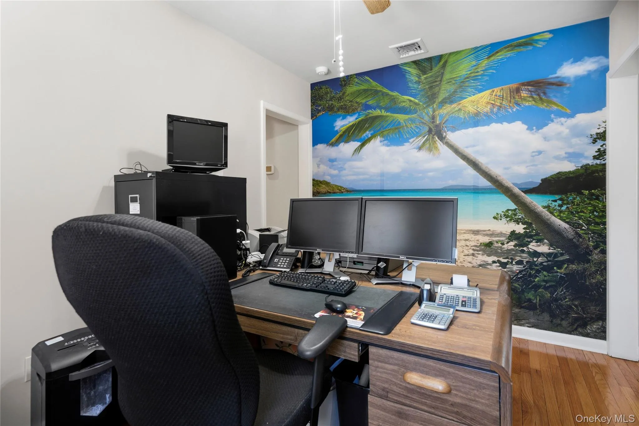Office space featuring wood-finish flooring, light-toned wall paint, and a decorative wall mural Office space featuring wood-finish flooring, light-toned wall paint, and a decorative wall mural