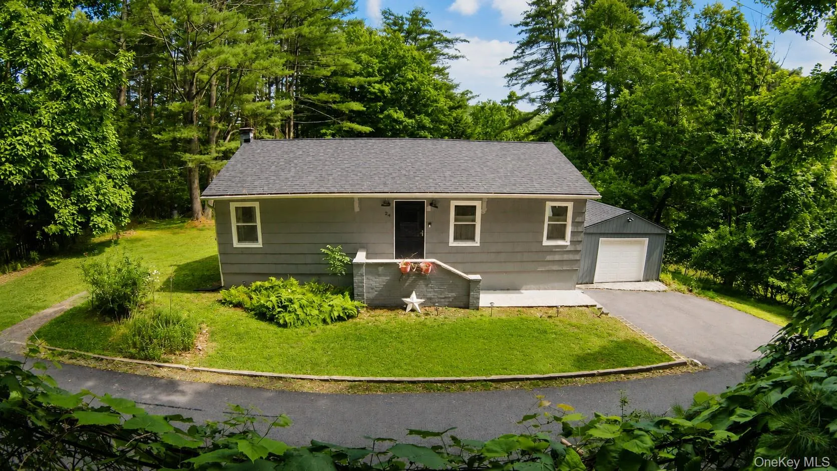 Located on a quiet road featuring a dark shingle roof, detached single-car garage, paved driveway, and established landscaping Located on a quiet road featuring a dark shingle roof, detached single-car garage, paved driveway, and established landscaping