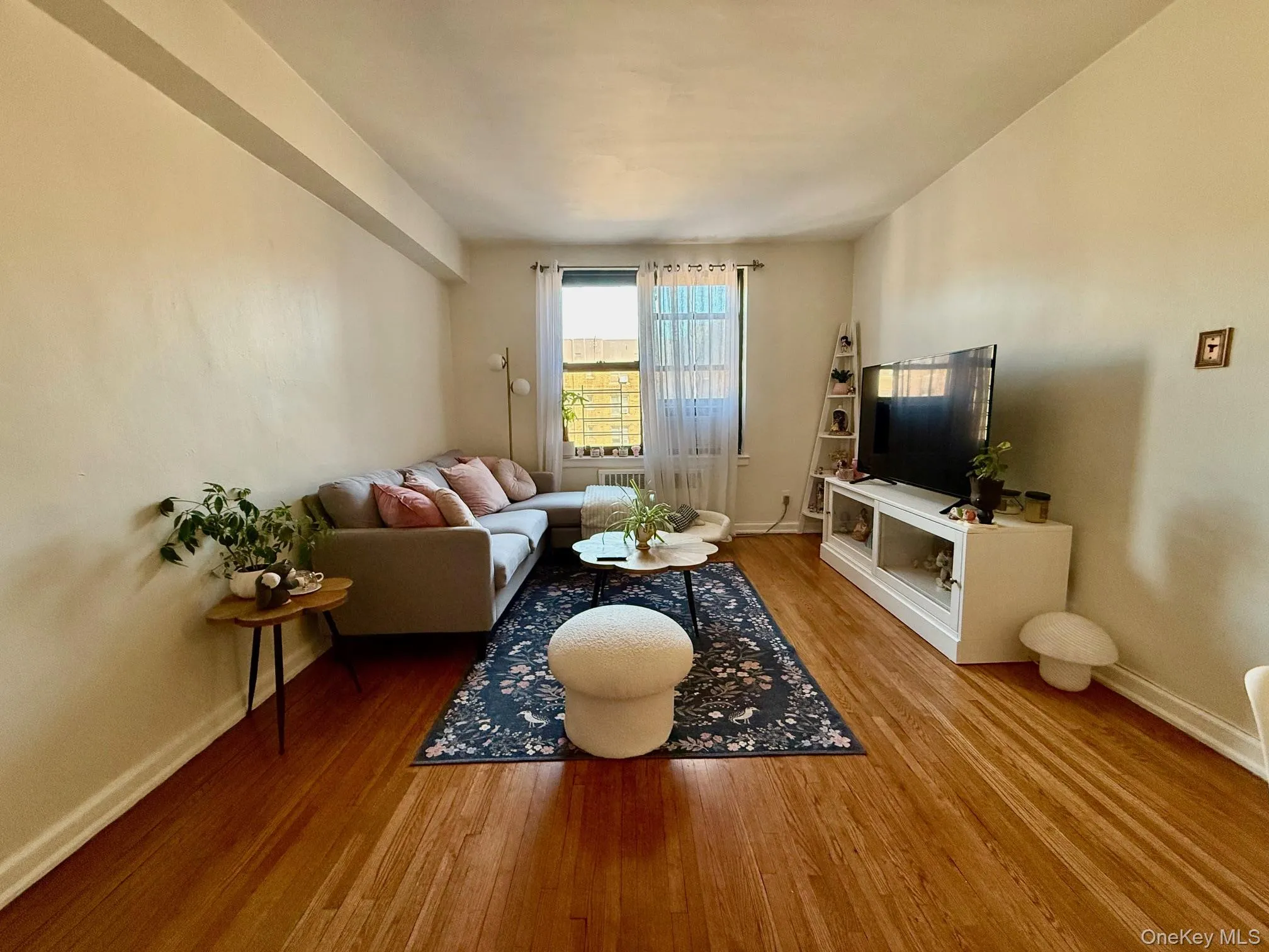 Bright living area featuring hardwood finish flooring, light toned wall finishes, and large double pane window Bright living area featuring hardwood finish flooring, light toned wall finishes, and large double pane window