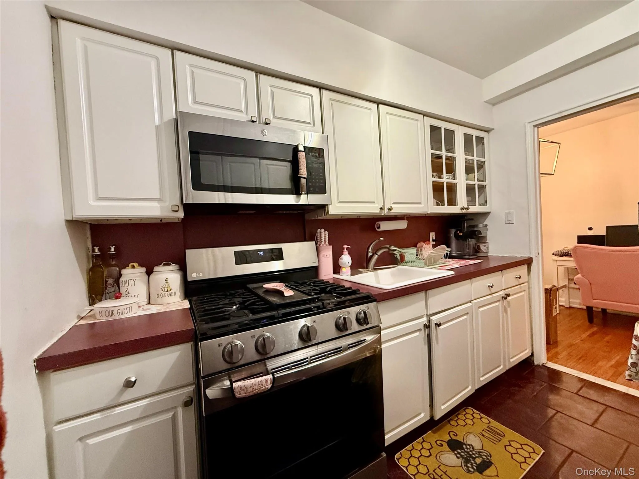Kitchen featuring white cabinetry, stainless steel appliances including a range and microwave, a white sink, and dark countertop surfaces Kitchen featuring white cabinetry, stainless steel appliances including a range and microwave, a white sink, and dark countertop surfaces