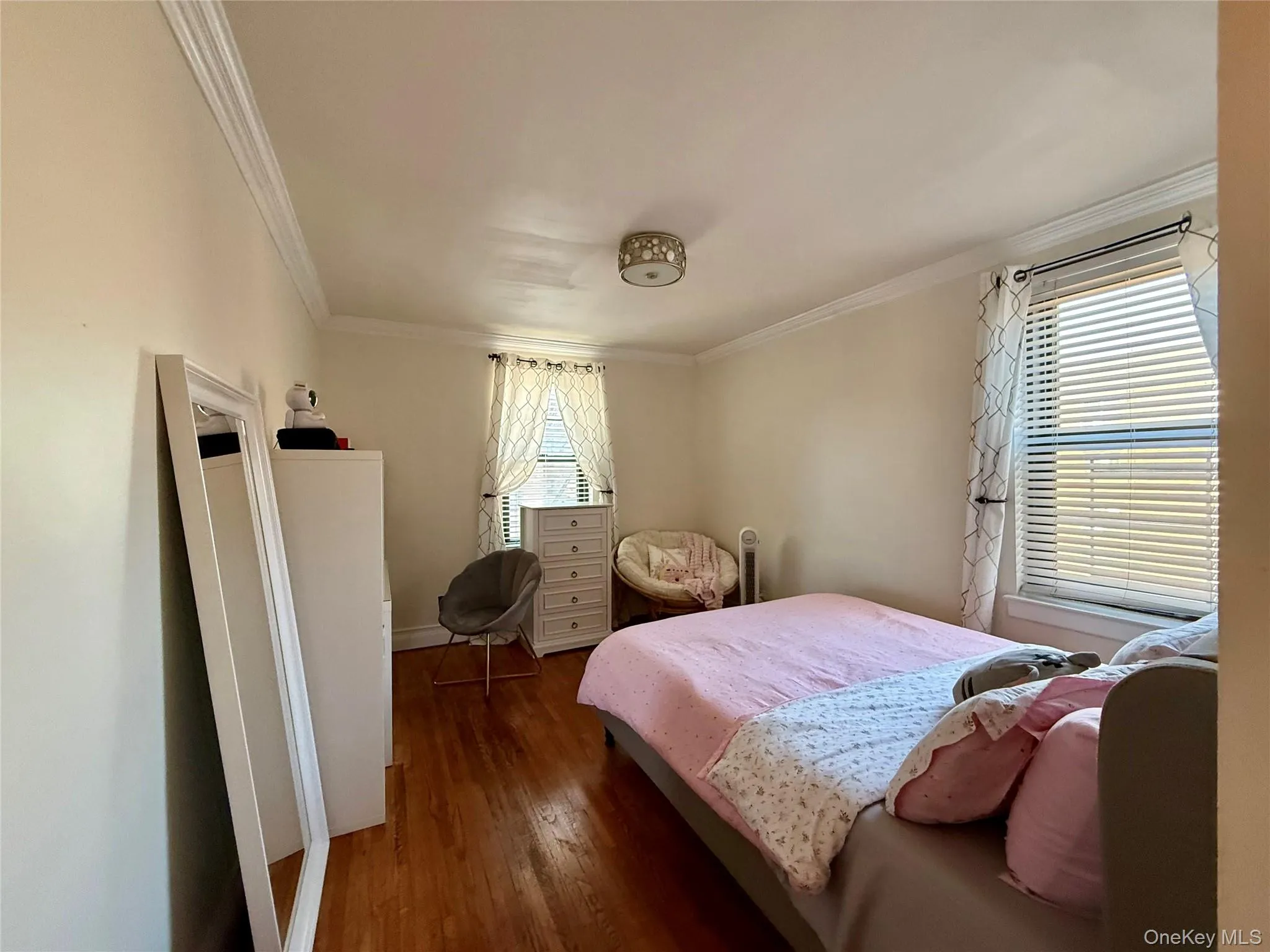 Bedroom featuring hardwood flooring, crown molding, a decorative ceiling light fixture, and two windows Bedroom featuring hardwood flooring, crown molding, a decorative ceiling light fixture, and two windows
