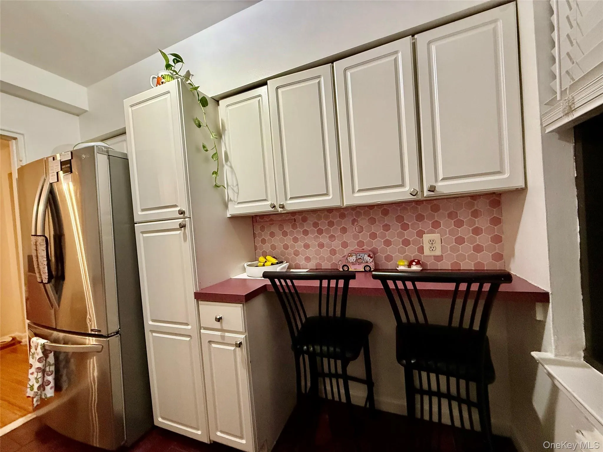 Modern kitchen featuring white shaker-style cabinetry, a pink hexagonal tile backsplash, and a built-in breakfast bar Modern kitchen featuring white shaker-style cabinetry, a pink hexagonal tile backsplash, and a built-in breakfast bar