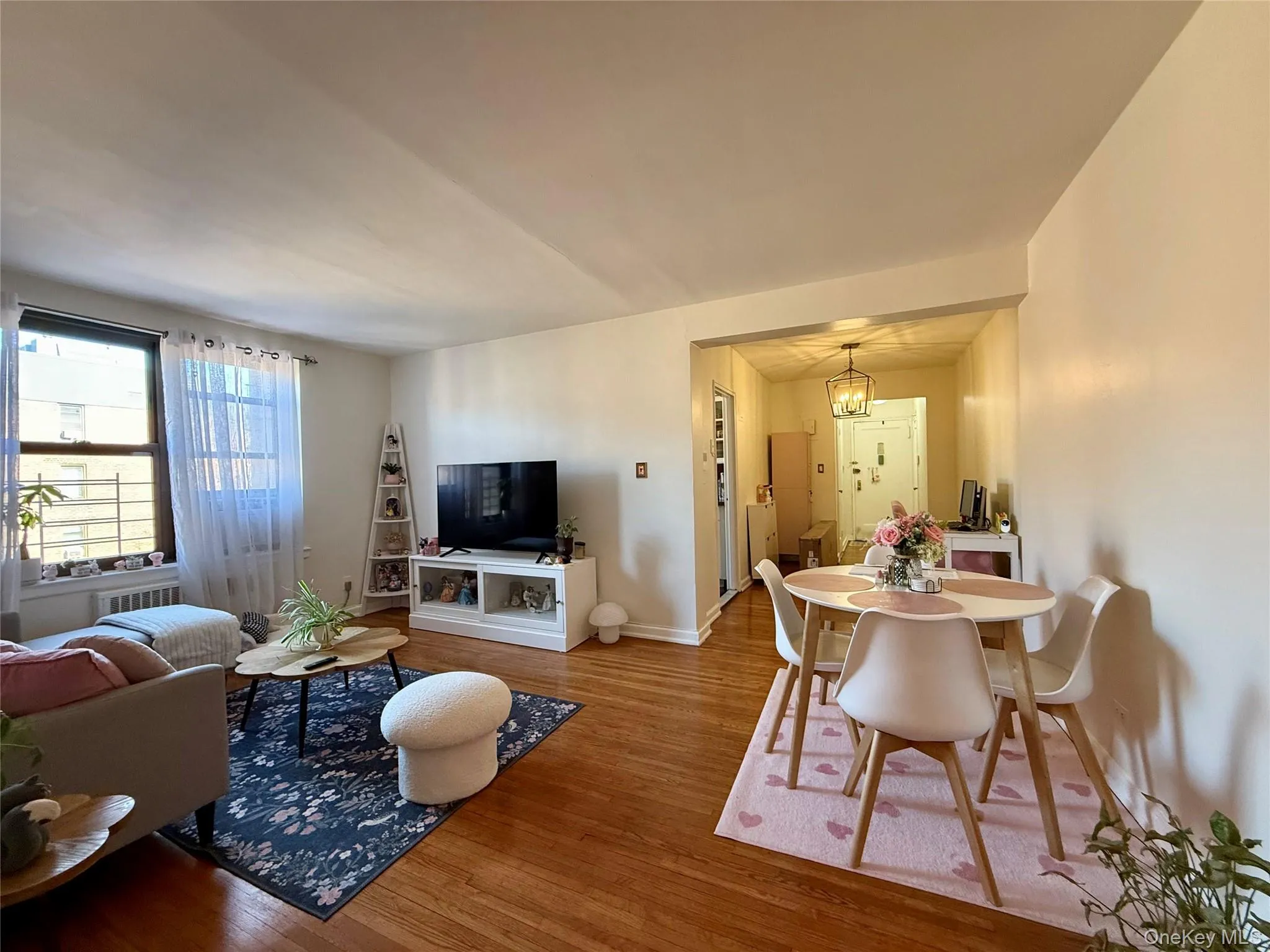 Living area featuring hardwood flooring, an elegant doorway, and ample natural light from a large window Living area featuring hardwood flooring, an elegant doorway, and ample natural light from a large window