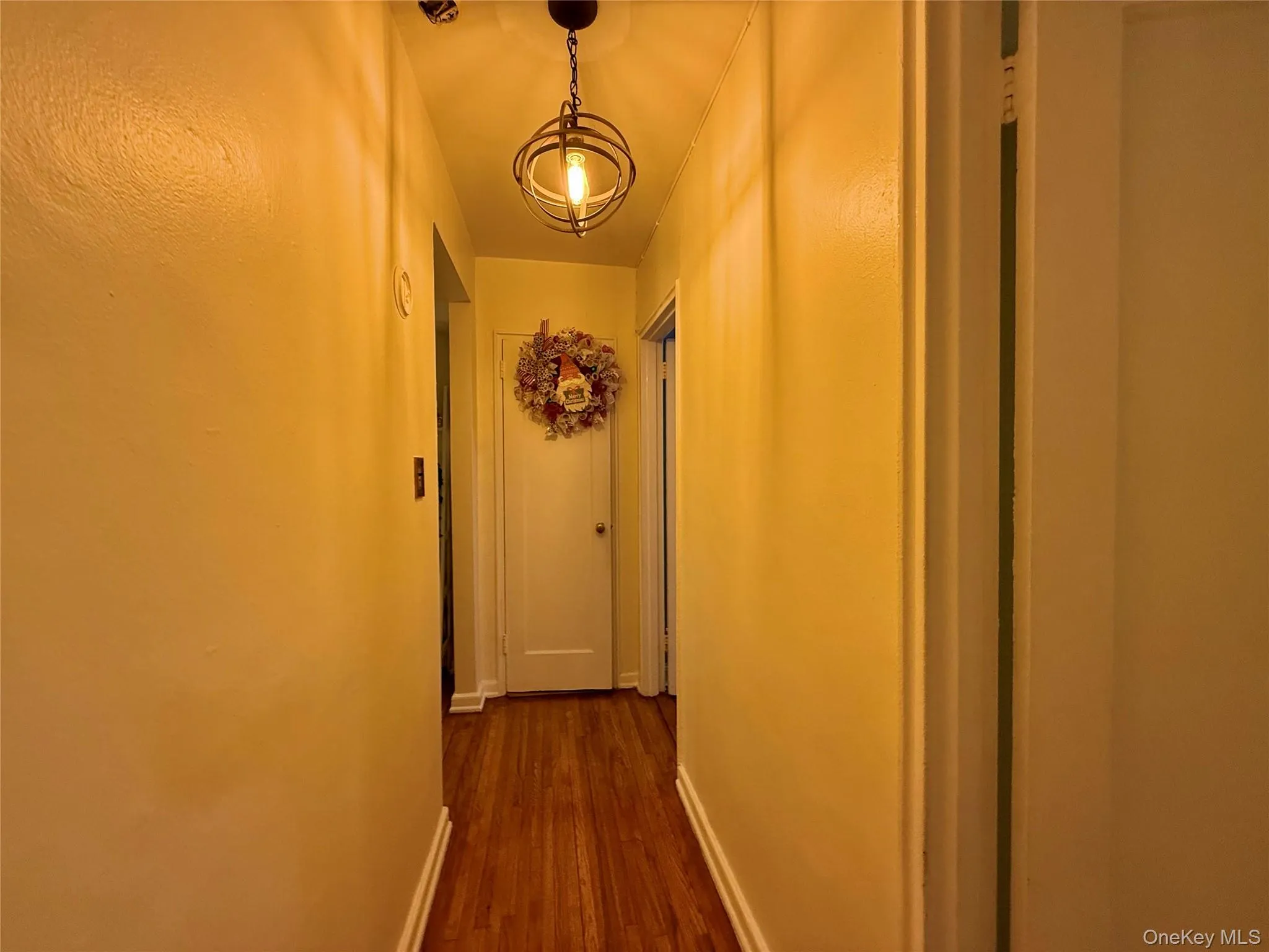 Hallway featuring hardwood finish flooring, a white paneled door, and two coat closets. Hallway featuring hardwood finish flooring, a white paneled door, and two coat closets.