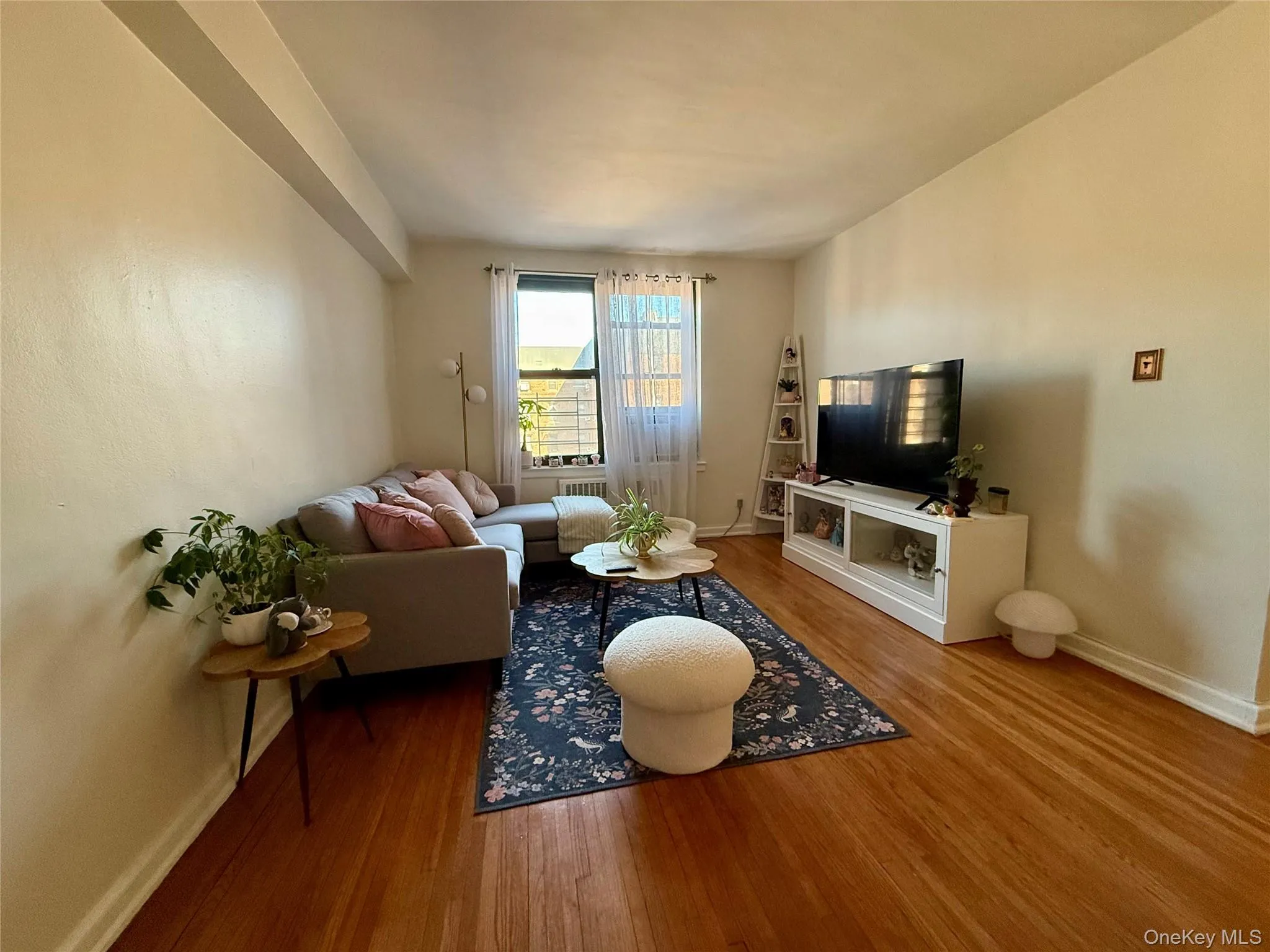 Living area featuring wood-finish flooring, light-toned walls, and a window with natural illumination Living area featuring wood-finish flooring, light-toned walls, and a window with natural illumination