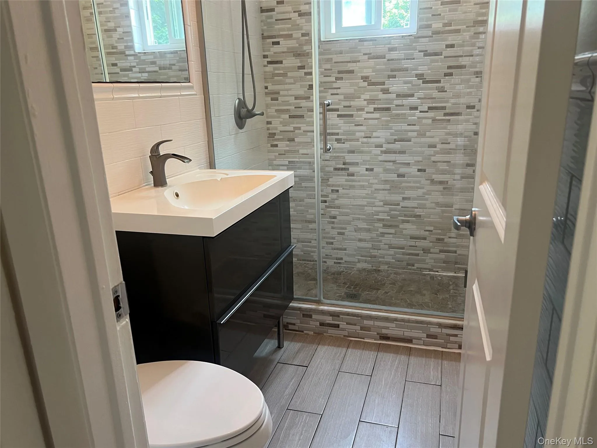 Modern bathroom featuring a dark wood-finish vanity with an integrated white sink, a matte black faucet, and a tiled shower enclosure with a glass door Modern bathroom featuring a dark wood-finish vanity with an integrated white sink, a matte black faucet, and a tiled shower enclosure with a glass door