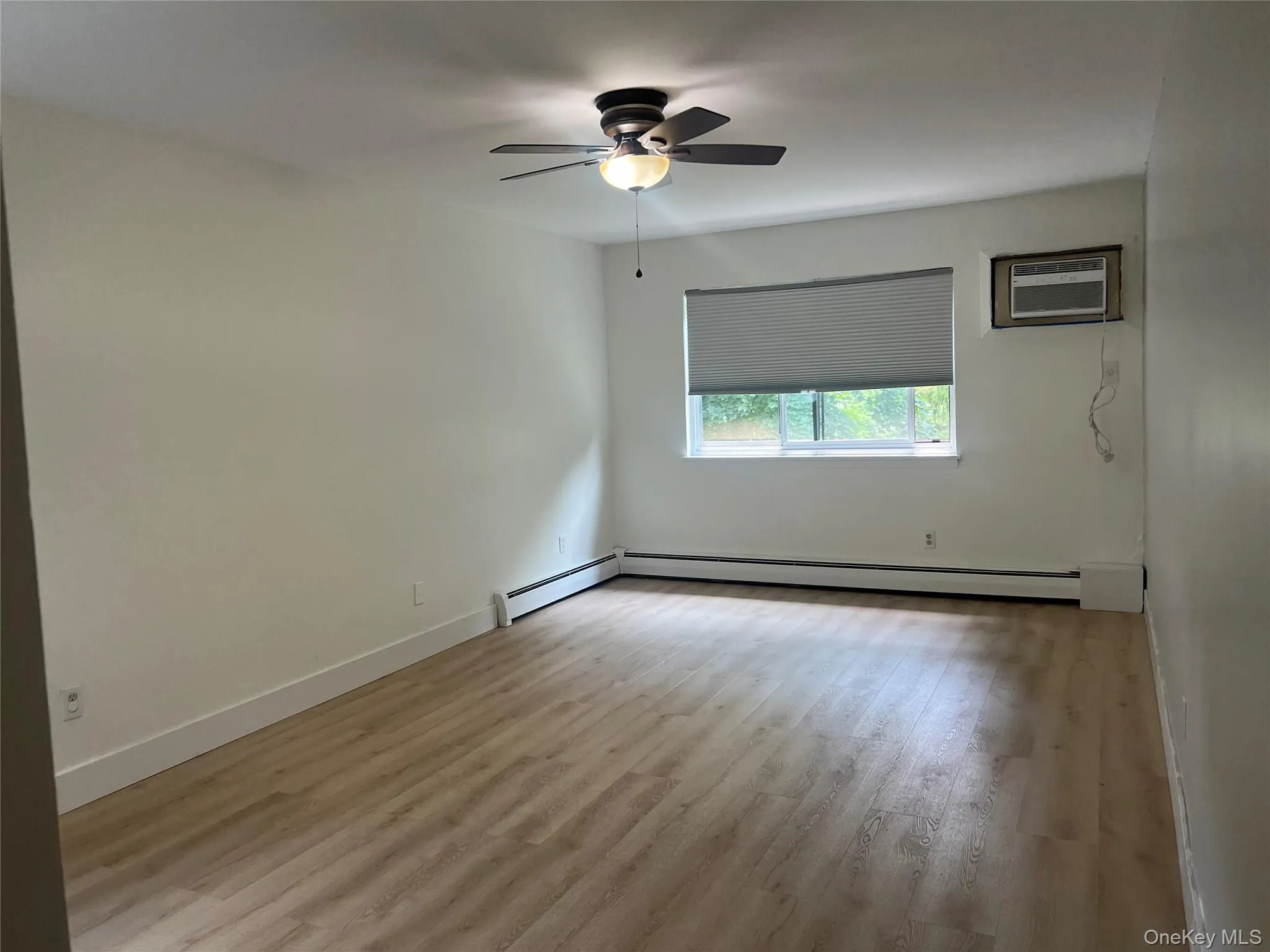 Spacious bedroom featuring wood-finish flooring and a ceiling fan with integrated lighting Spacious bedroom featuring wood-finish flooring and a ceiling fan with integrated lighting