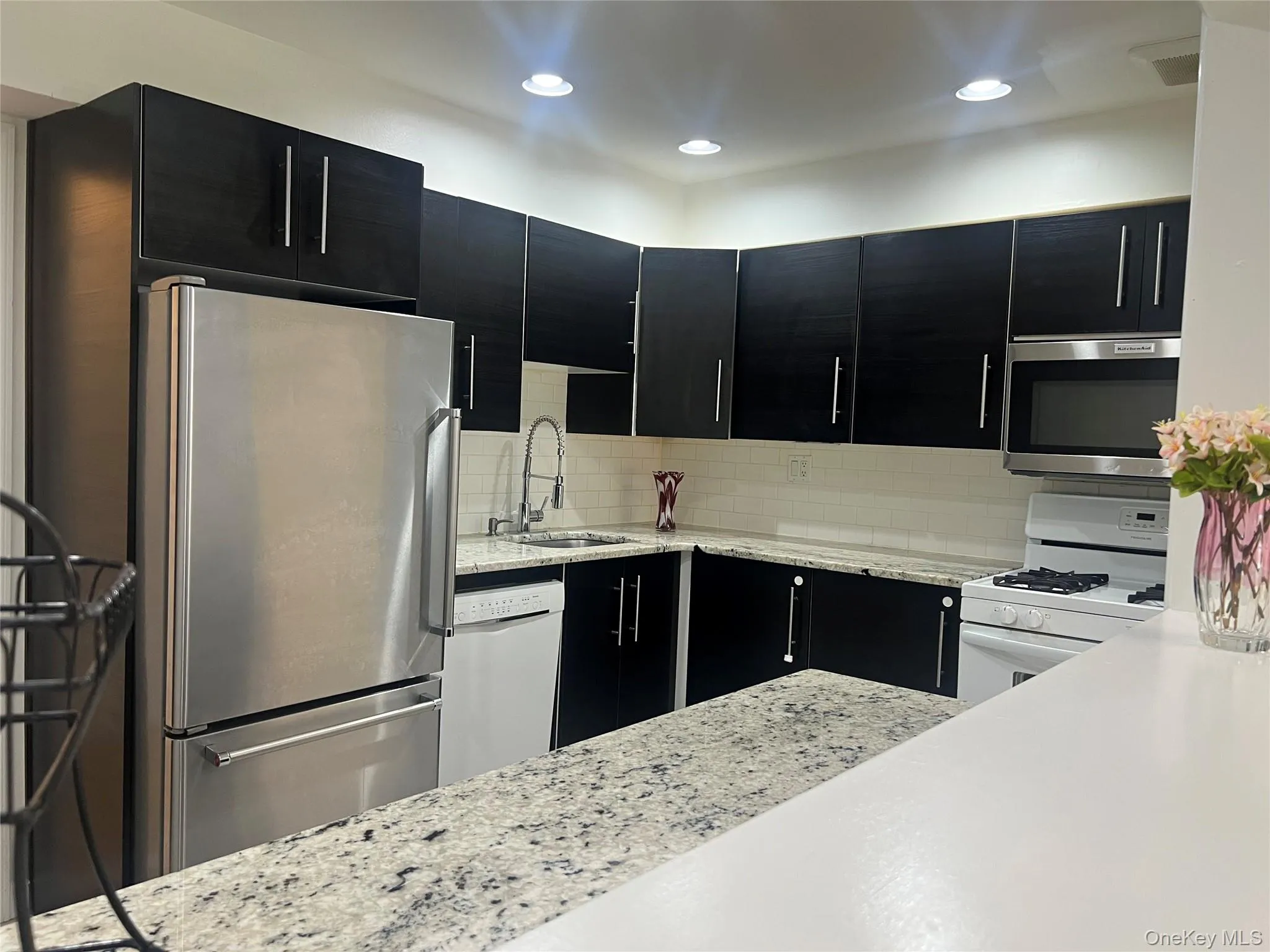 Contemporary kitchen featuring dark cabinetry, speckled countertops, stainless steel appliances, and recessed lighting Contemporary kitchen featuring dark cabinetry, speckled countertops, stainless steel appliances, and recessed lighting