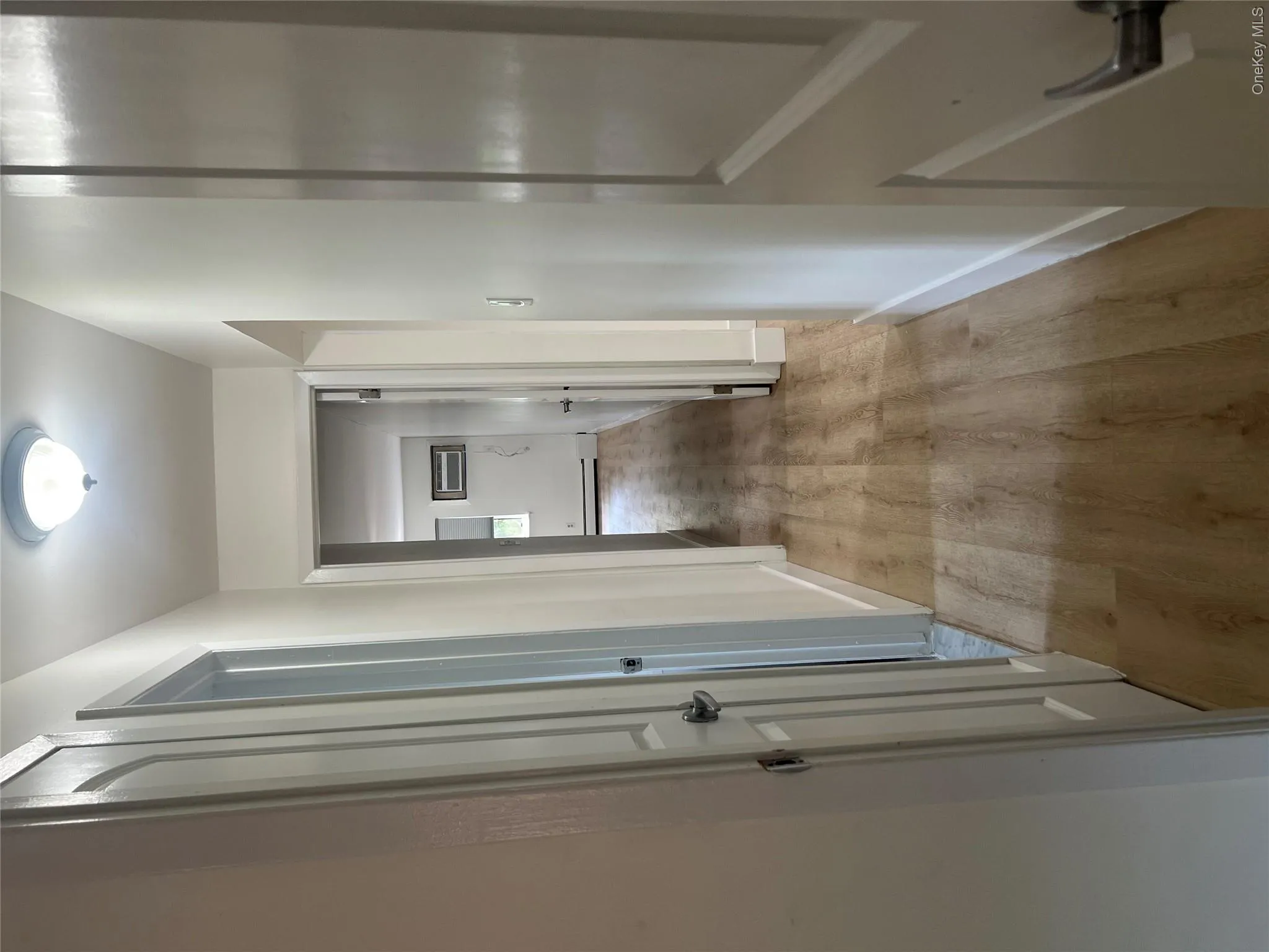 Interior hallway featuring wood-finish flooring, white painted walls, and a ceiling-mounted light fixture Interior hallway featuring wood-finish flooring, white painted walls, and a ceiling-mounted light fixture