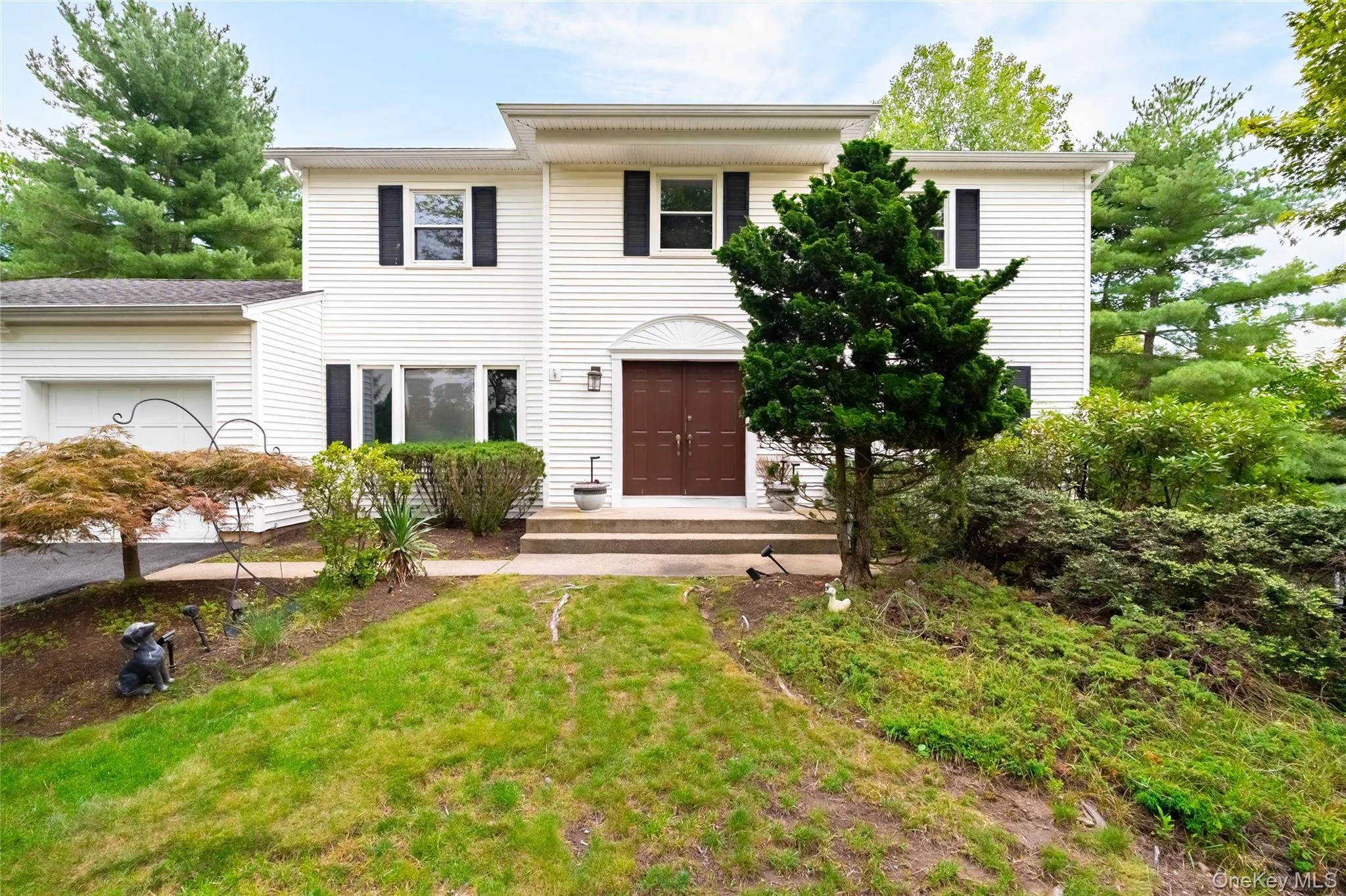 White siding exterior with dark shutters, a two-car garage, and a brown double entry door White siding exterior with dark shutters, a two-car garage, and a brown double entry door