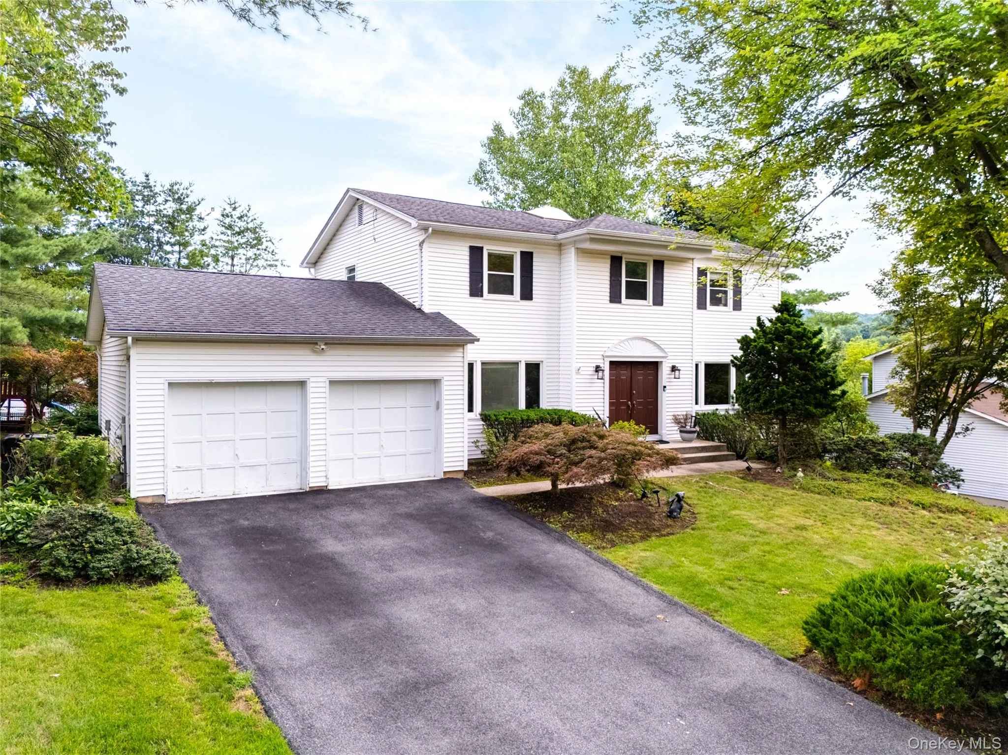 White siding exterior with a two-car garage, asphalt driveway, mature trees, and a landscaped front yard White siding exterior with a two-car garage, asphalt driveway, mature trees, and a landscaped front yard