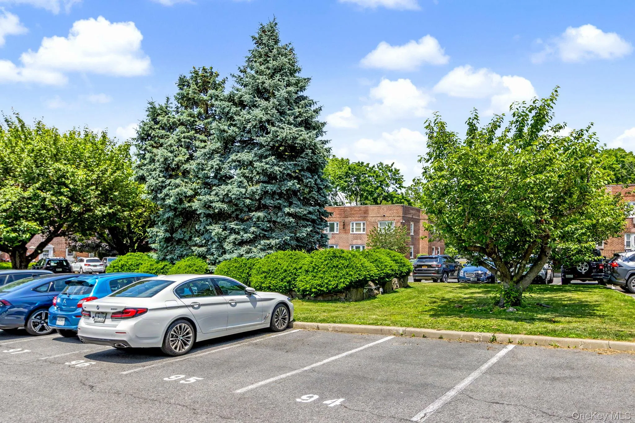 Paved parking lot featuring designated parking spaces, surrounded by manicured green spaces and mature trees Paved parking lot featuring designated parking spaces, surrounded by manicured green spaces and mature trees