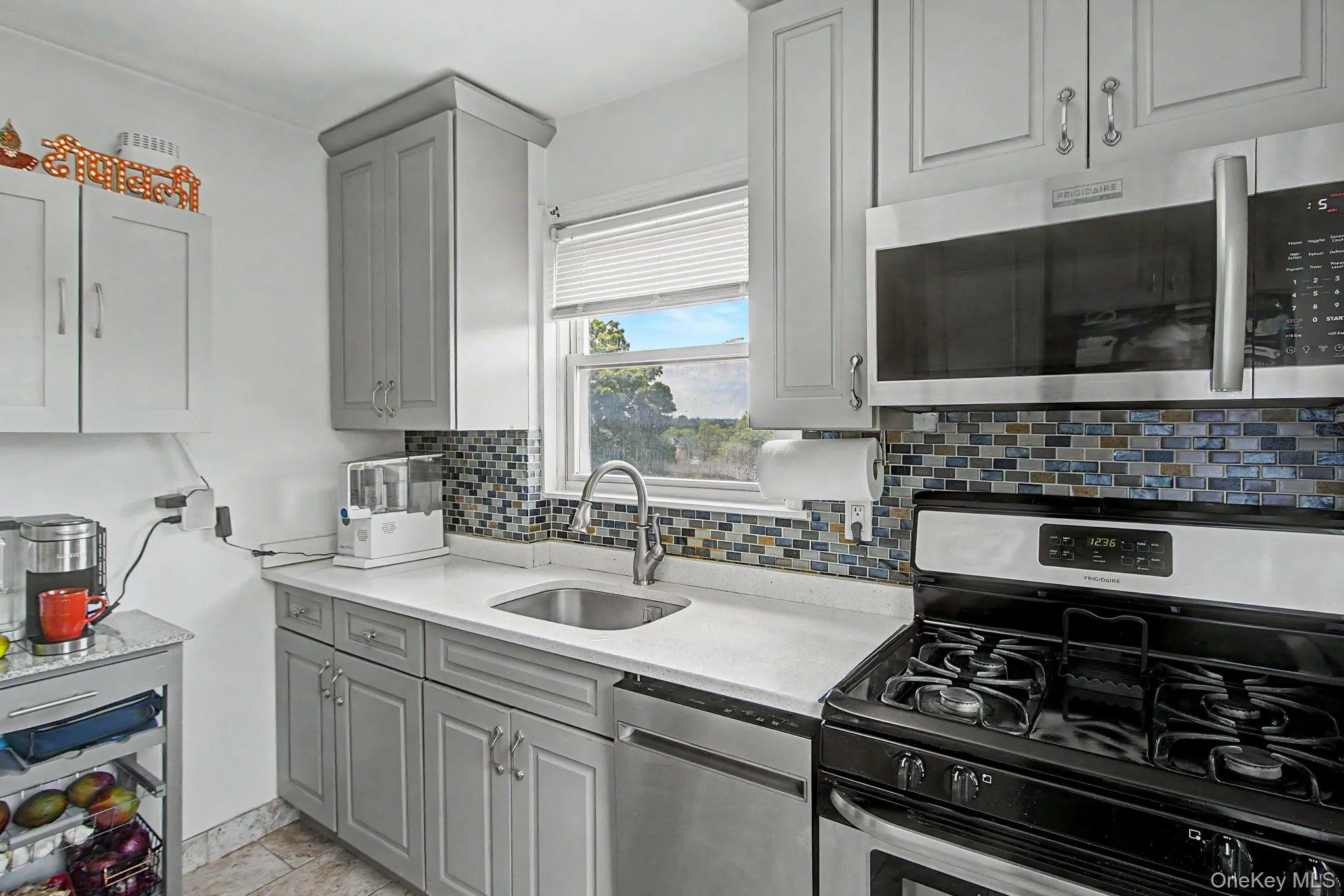 Modern kitchen featuring light gray cabinetry, a mosaic tile backsplash, a stainless steel sink with a gooseneck faucet, a built-in microwave, and a gas range Modern kitchen featuring light gray cabinetry, a mosaic tile backsplash, a stainless steel sink with a gooseneck faucet, a built-in microwave, and a gas range