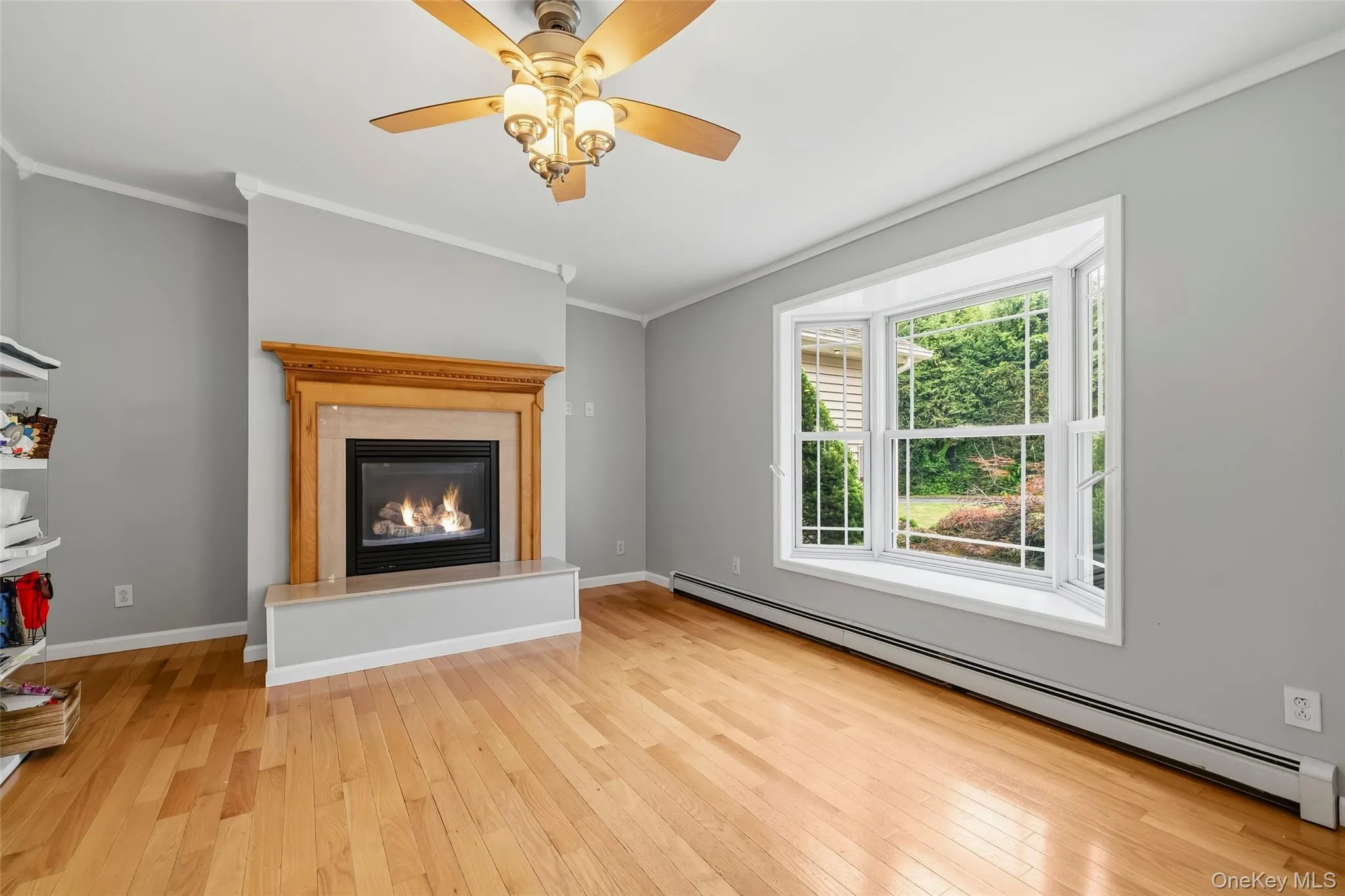 Living area featuring a gas fireplace with a wood mantle and stone surround, a bay window, wood-finish flooring, and crown molding Living area featuring a gas fireplace with a wood mantle and stone surround, a bay window, wood-finish flooring, and crown molding