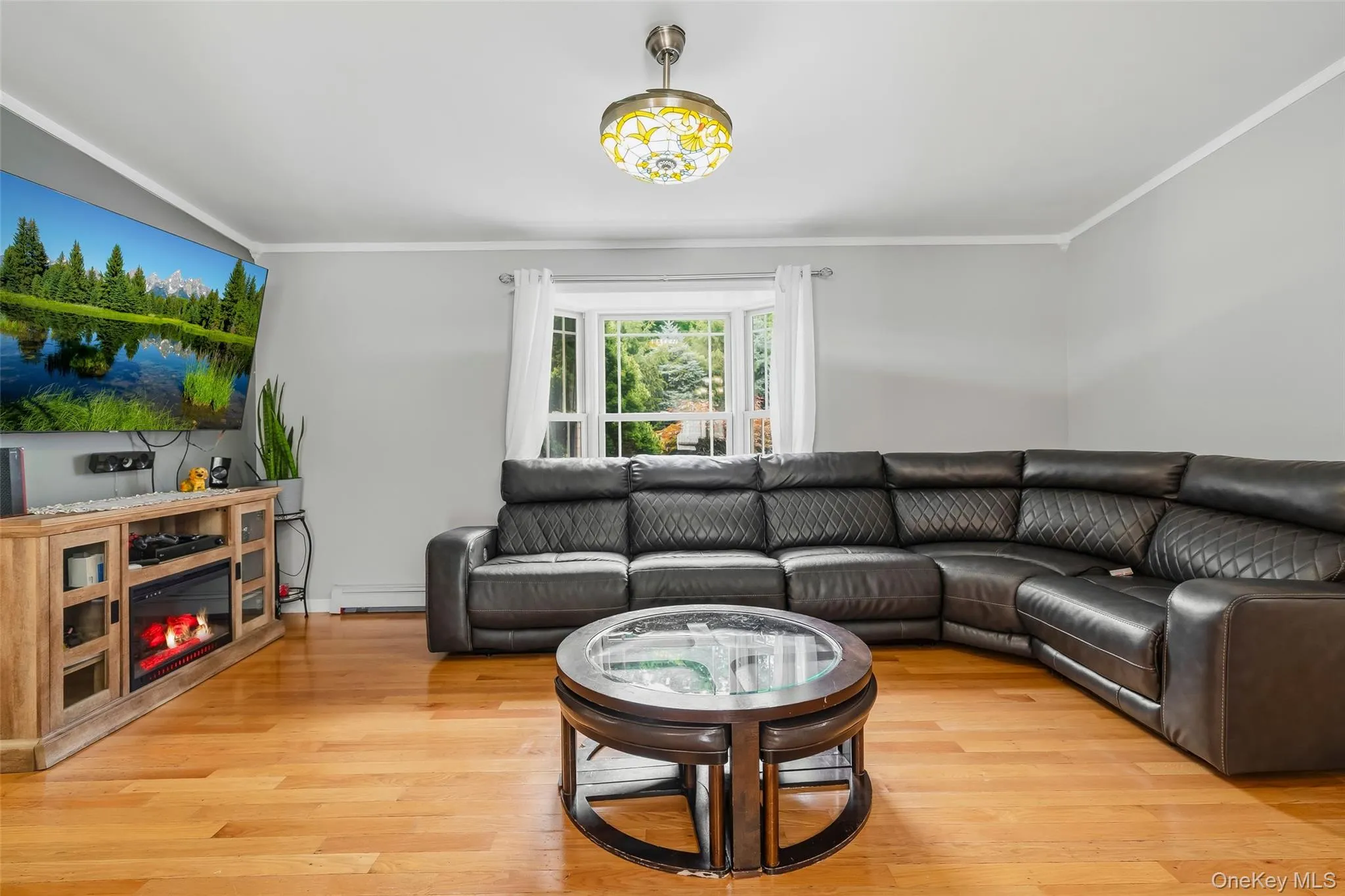 Living area featuring wood-finish flooring, a bay window with natural light, light gray wall paint, and white crown molding Living area featuring wood-finish flooring, a bay window with natural light, light gray wall paint, and white crown molding