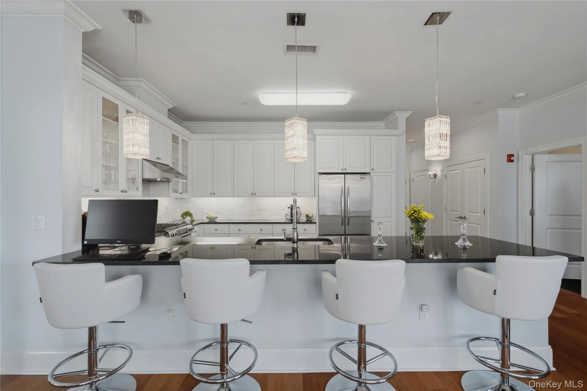 Alternate view of the kitchen, showcasing elegant pendant lighting, stainless steel appliances, and seating for four at the breakfast bar. Alternate view of the kitchen, showcasing elegant pendant lighting, stainless steel appliances, and seating for four at the breakfast bar.