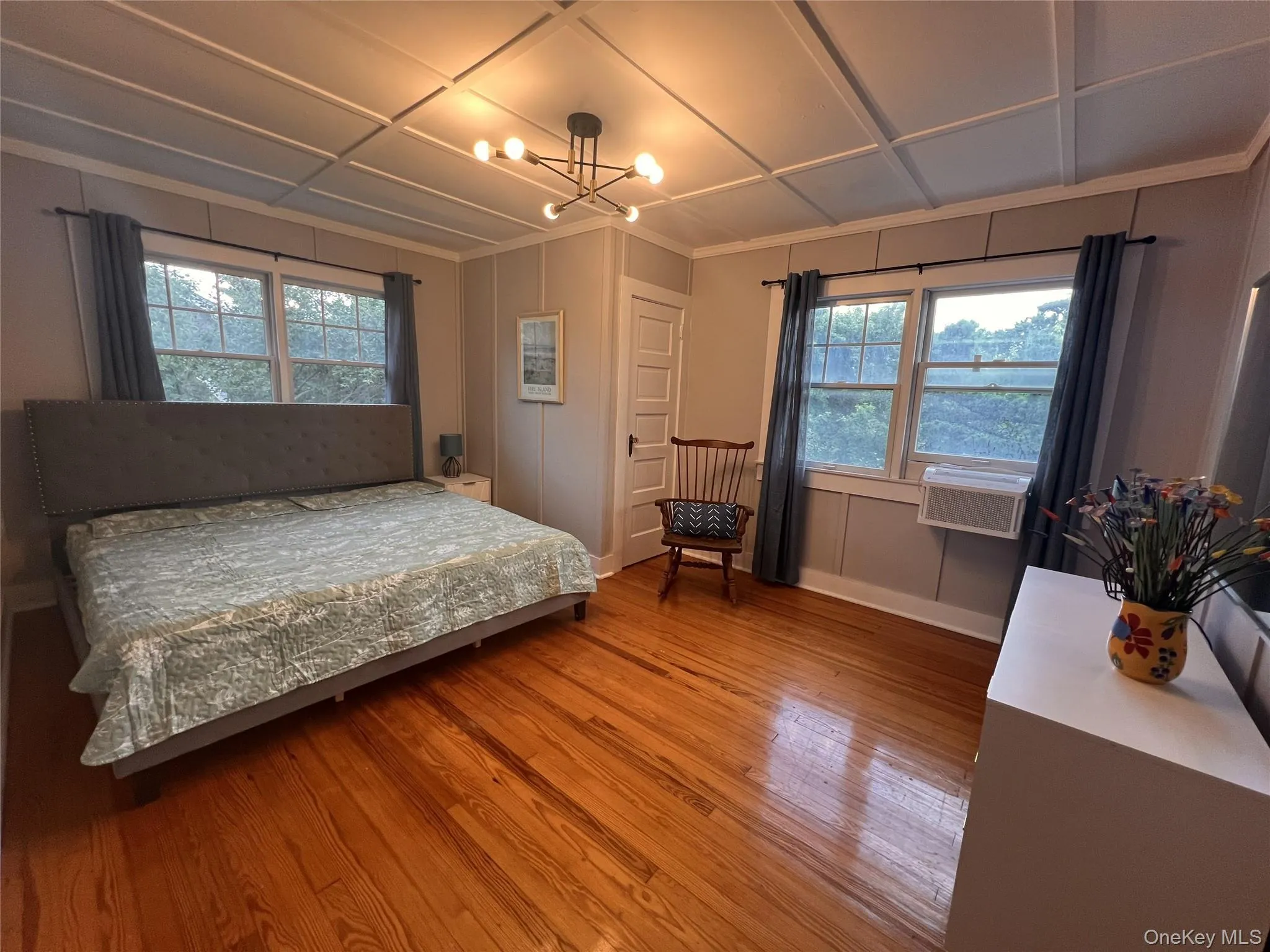Bedroom featuring wood finished floors, multiple windows, and a chandelier Bedroom featuring wood finished floors, multiple windows, and a chandelier
