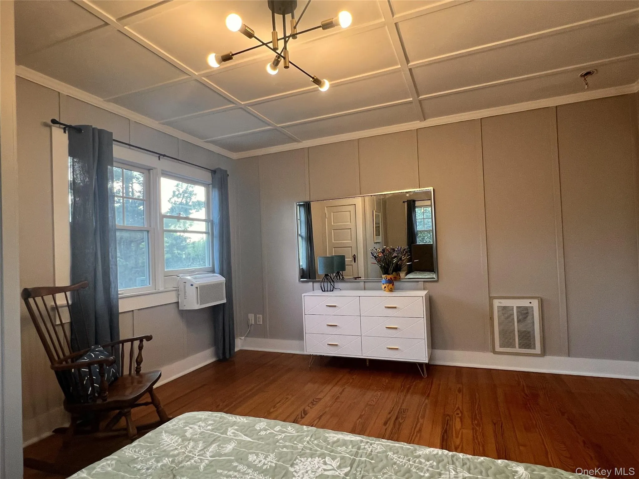 Bedroom featuring dark wood-type flooring, a chandelier, a decorative wall, heating unit, and crown molding Bedroom featuring dark wood-type flooring, a chandelier, a decorative wall, heating unit, and crown molding