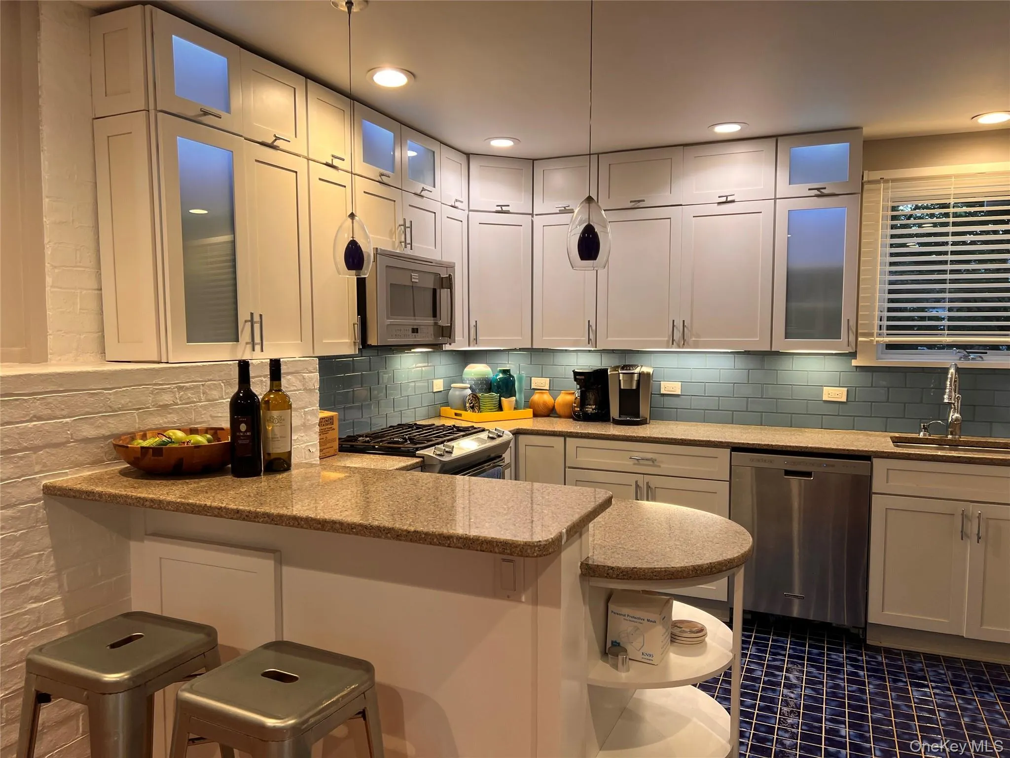 Kitchen with a peninsula, stainless steel appliances, a kitchen bar, decorative backsplash, and light stone countertops Kitchen with a peninsula, stainless steel appliances, a kitchen bar, decorative backsplash, and light stone countertops