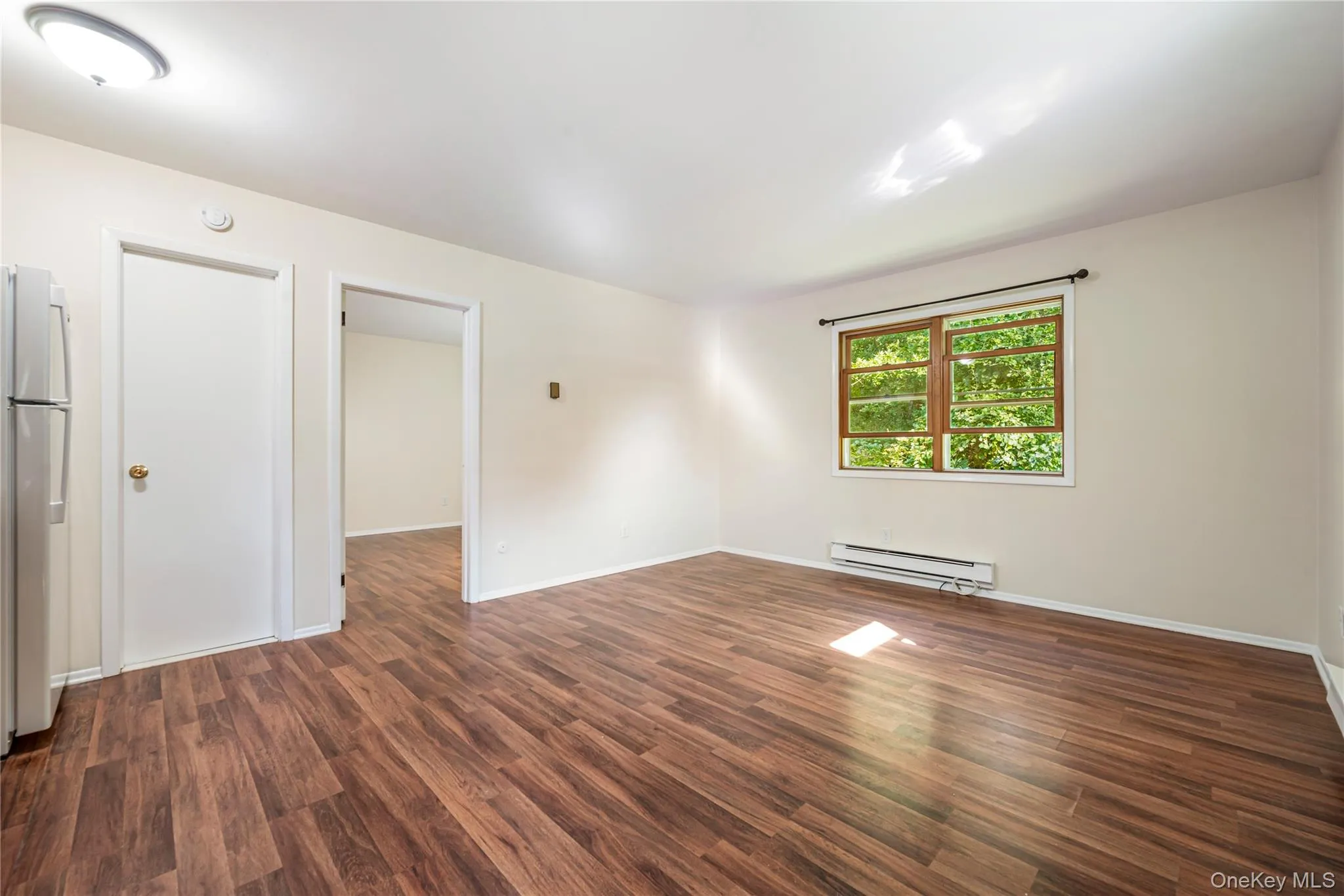 Empty room with baseboard heating and dark hardwood / wood-style flooring Empty room with baseboard heating and dark hardwood / wood-style flooring