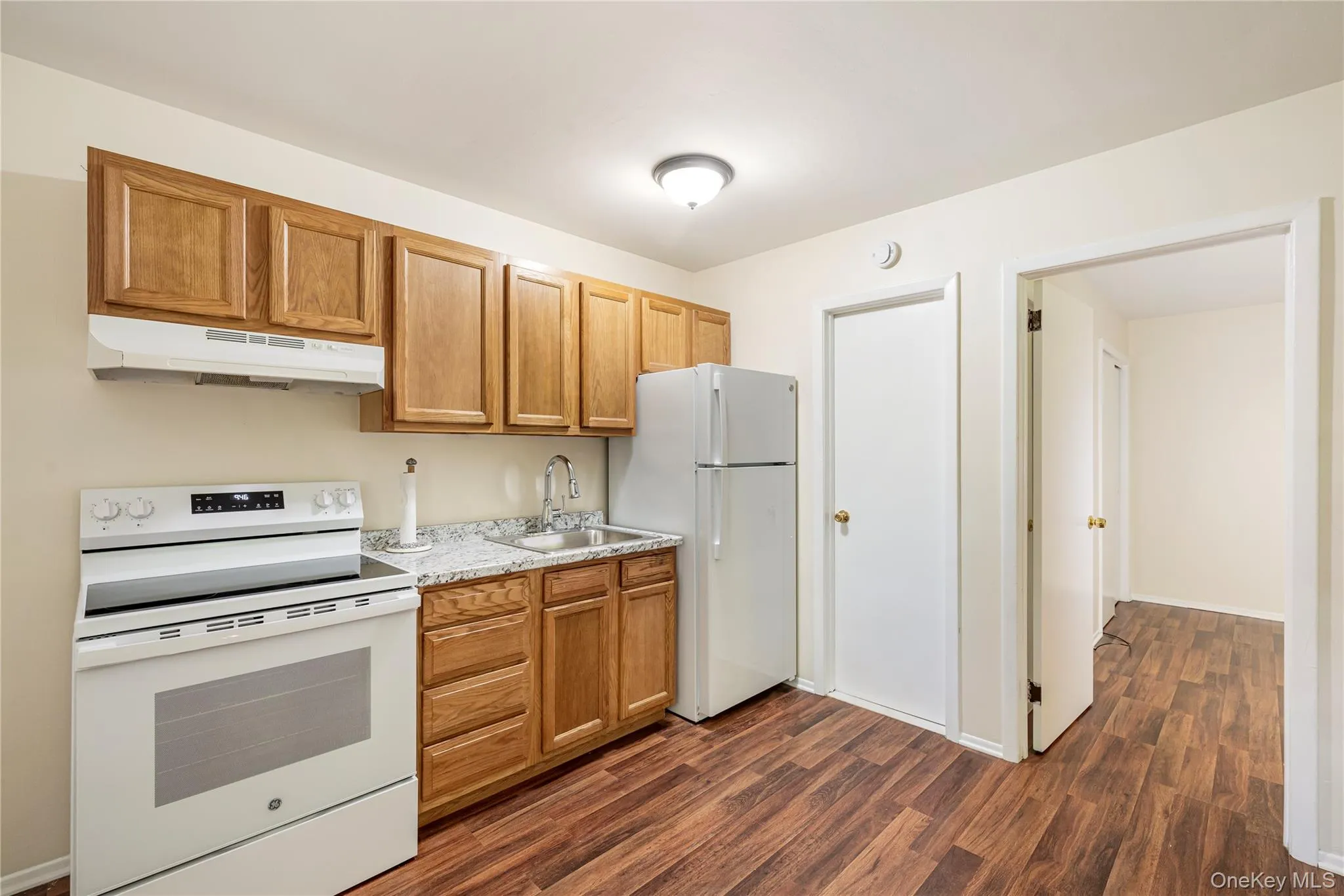 Kitchen with light counters, sink, white appliances, and dark hardwood / wood-style floors Kitchen with light counters, sink, white appliances, and dark hardwood / wood-style floors