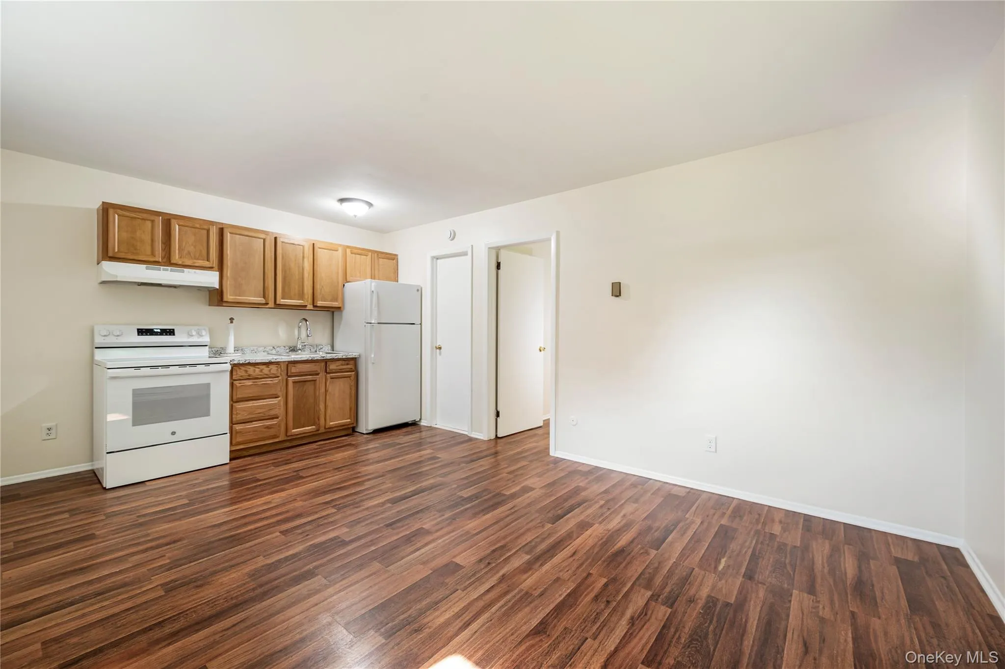 Kitchen with dark wood-type flooring, sink, and white appliances Kitchen with dark wood-type flooring, sink, and white appliances