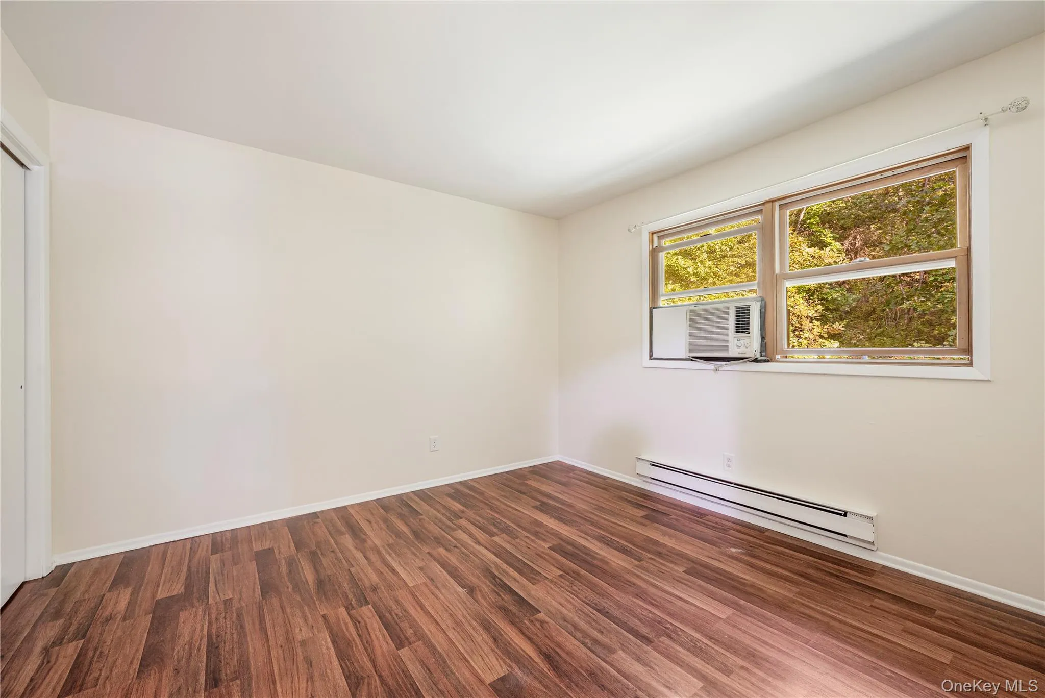 Unfurnished room with dark hardwood / wood-style flooring and a baseboard heating unit Unfurnished room with dark hardwood / wood-style flooring and a baseboard heating unit