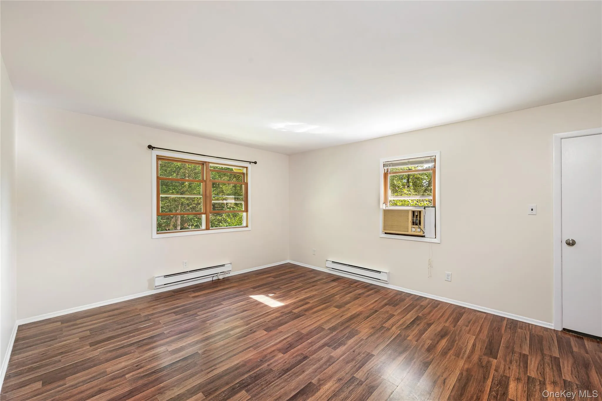 Unfurnished room featuring dark hardwood / wood-style flooring and a baseboard heating unit Unfurnished room featuring dark hardwood / wood-style flooring and a baseboard heating unit