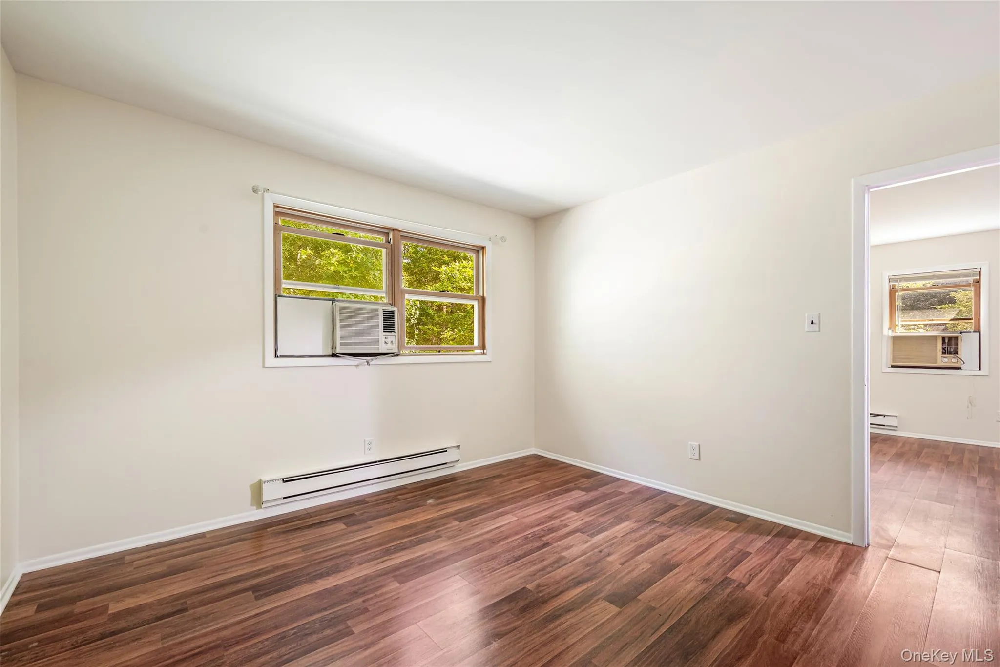 Empty room featuring baseboard heating, a healthy amount of sunlight, and dark hardwood / wood-style floors Empty room featuring baseboard heating, a healthy amount of sunlight, and dark hardwood / wood-style floors