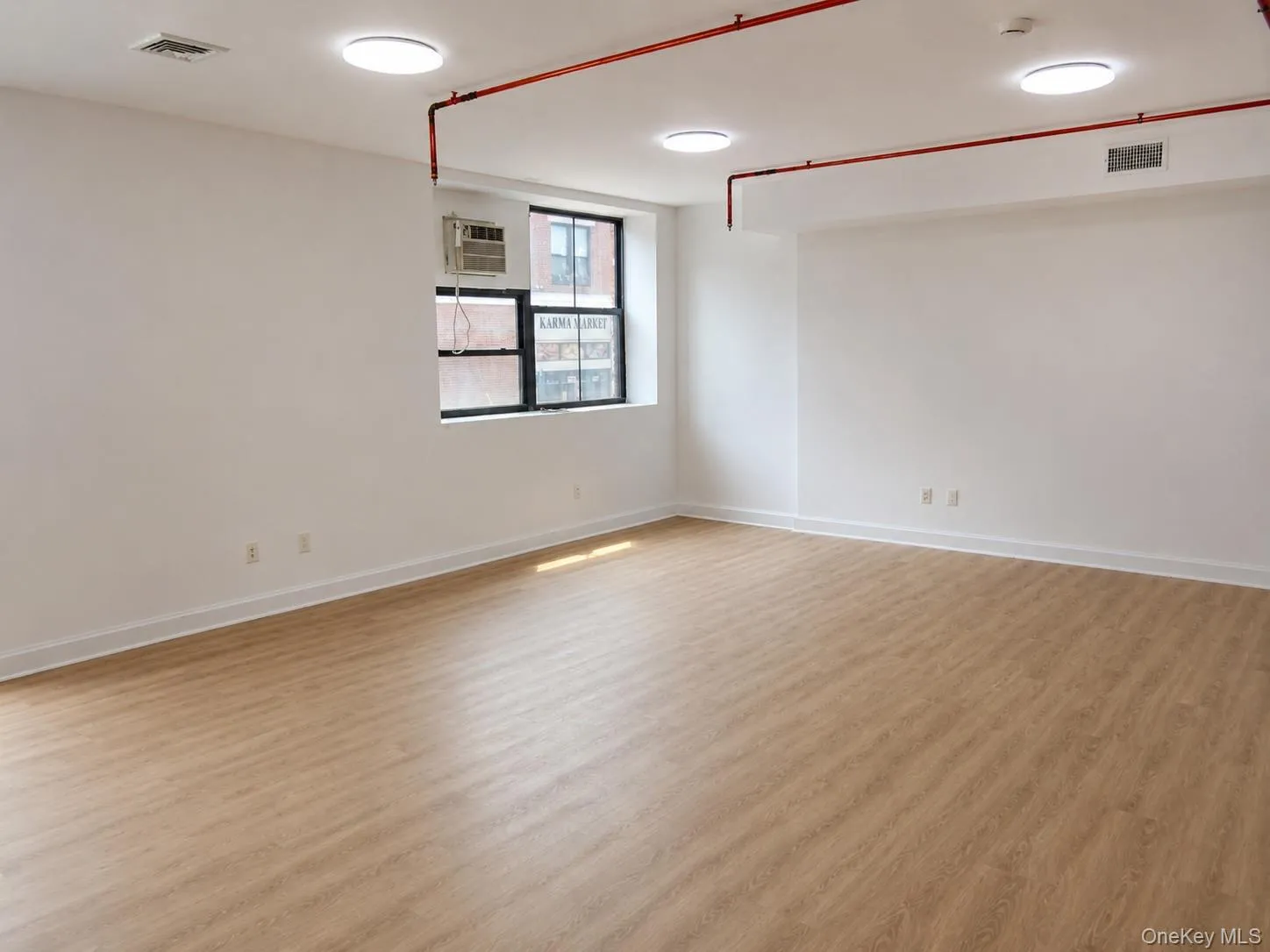 Spacious room featuring wood-finish flooring, white walls, and multiple recessed ceiling lights Spacious room featuring wood-finish flooring, white walls, and multiple recessed ceiling lights
