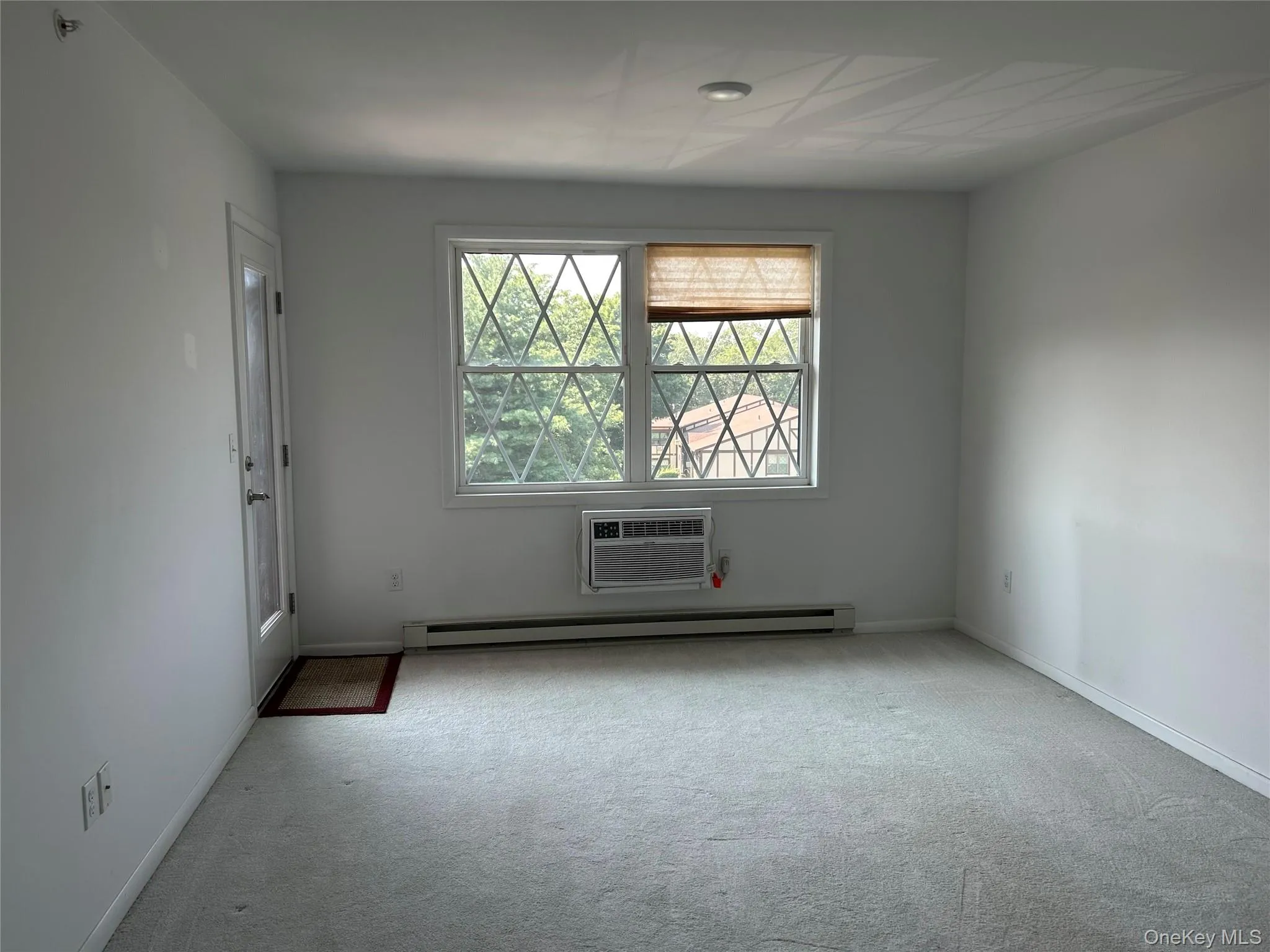 Empty room featuring carpet, baseboard heating, and a wall mounted AC Empty room featuring carpet, baseboard heating, and a wall mounted AC