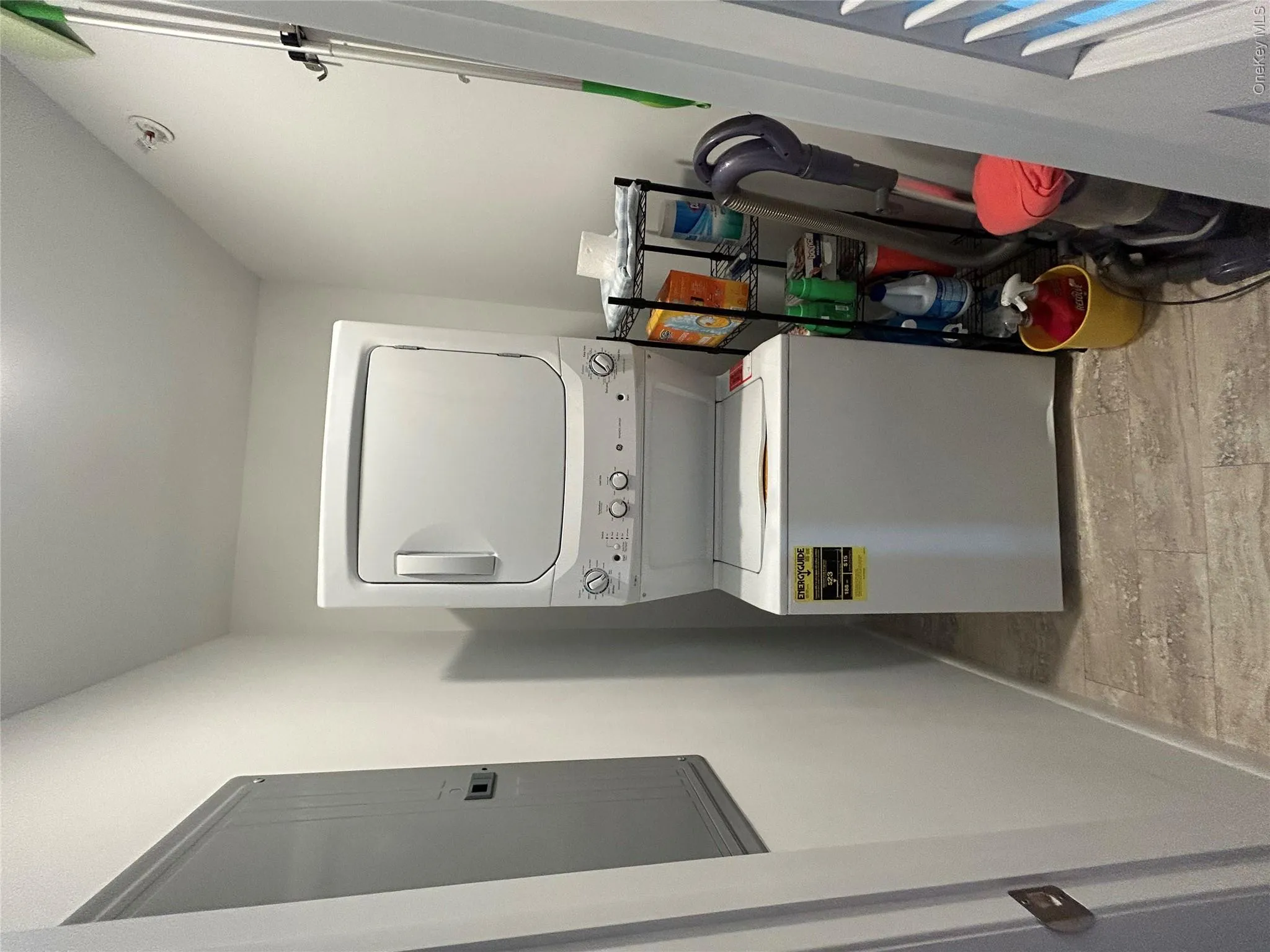 Washroom featuring stacked washer and clothes dryer, electric panel, and light wood-style floors Washroom featuring stacked washer and clothes dryer, electric panel, and light wood-style floors