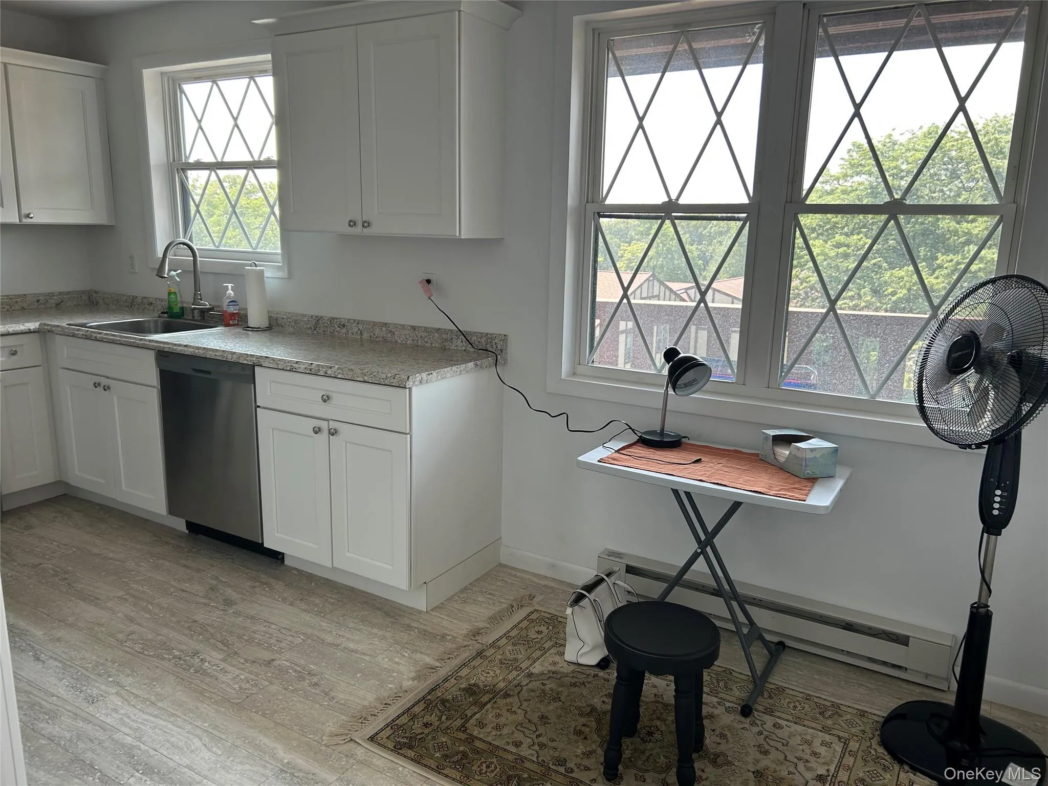 Kitchen featuring baseboard heating, light wood finished floors, stainless steel dishwasher, and white cabinets Kitchen featuring baseboard heating, light wood finished floors, stainless steel dishwasher, and white cabinets